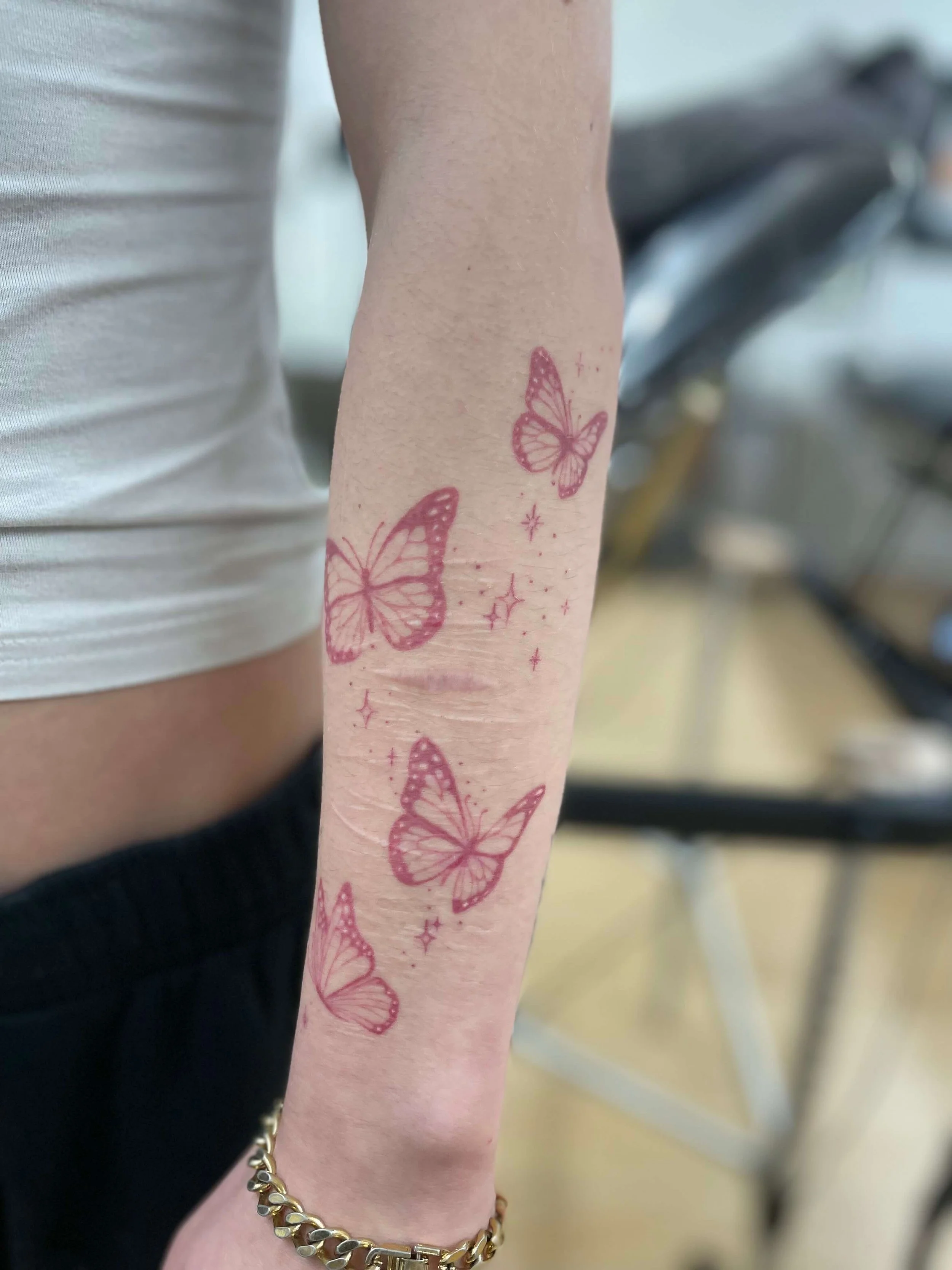 Forearm tattoo of pink butterflies and sparkle effects.