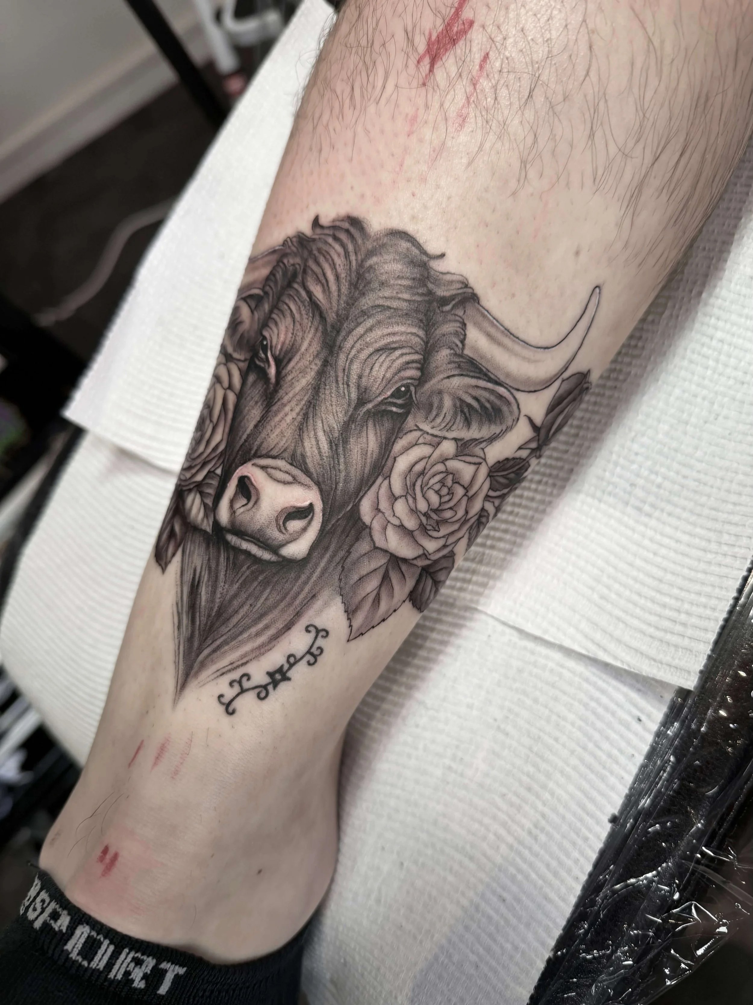 Black and gray tattoo of a bison head with a rose and decorative elements on a person's forearm.