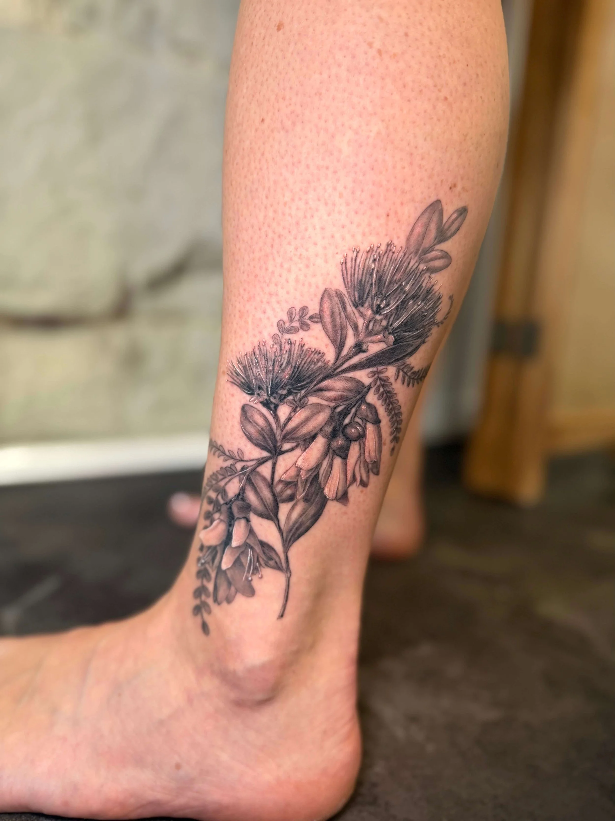 Black and gray floral tattoo on a person's lower leg, featuring detailed flowers and leaves.