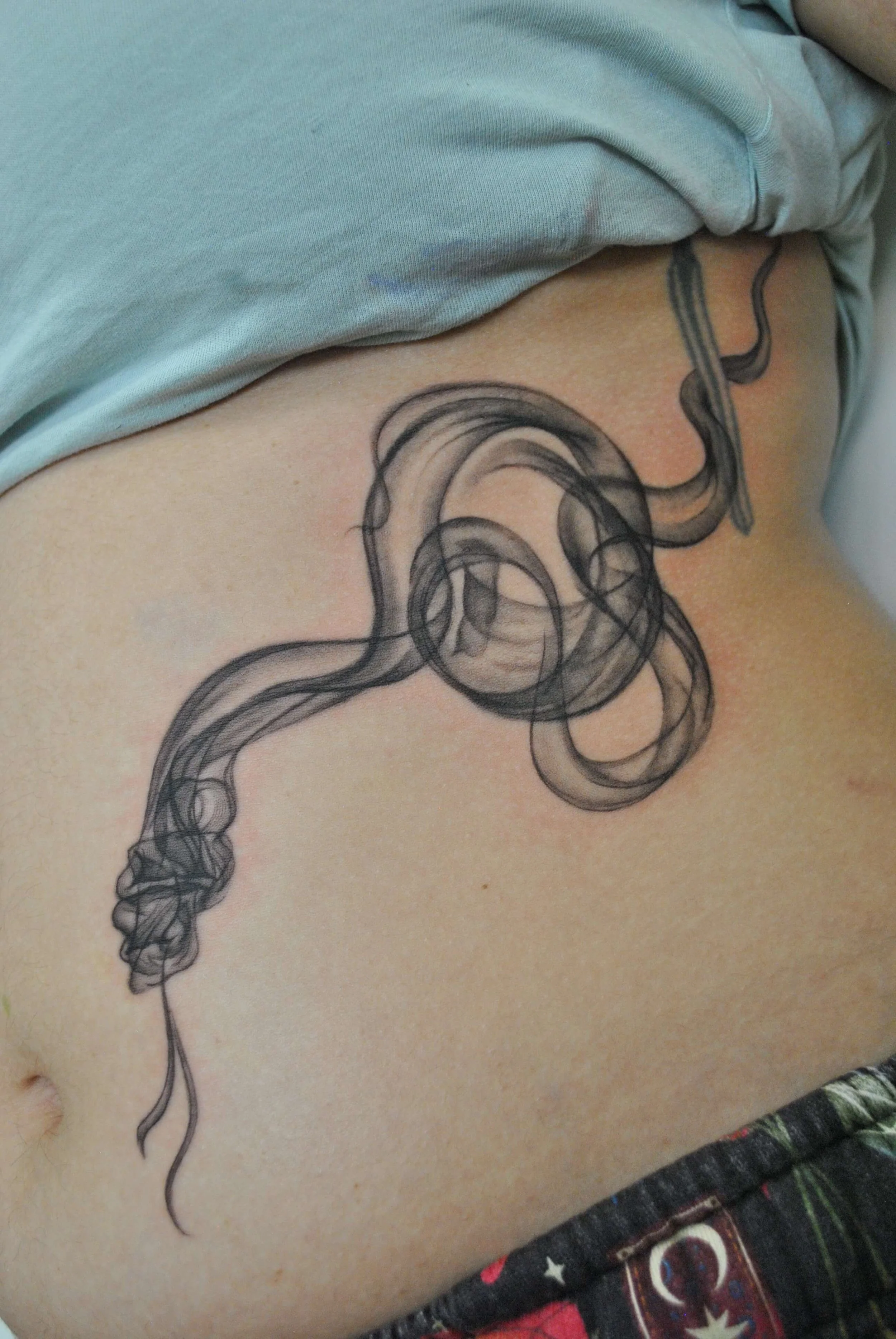 A black tattoo of a smoking pipe with swirling smoke on lower side of person's abdomen.