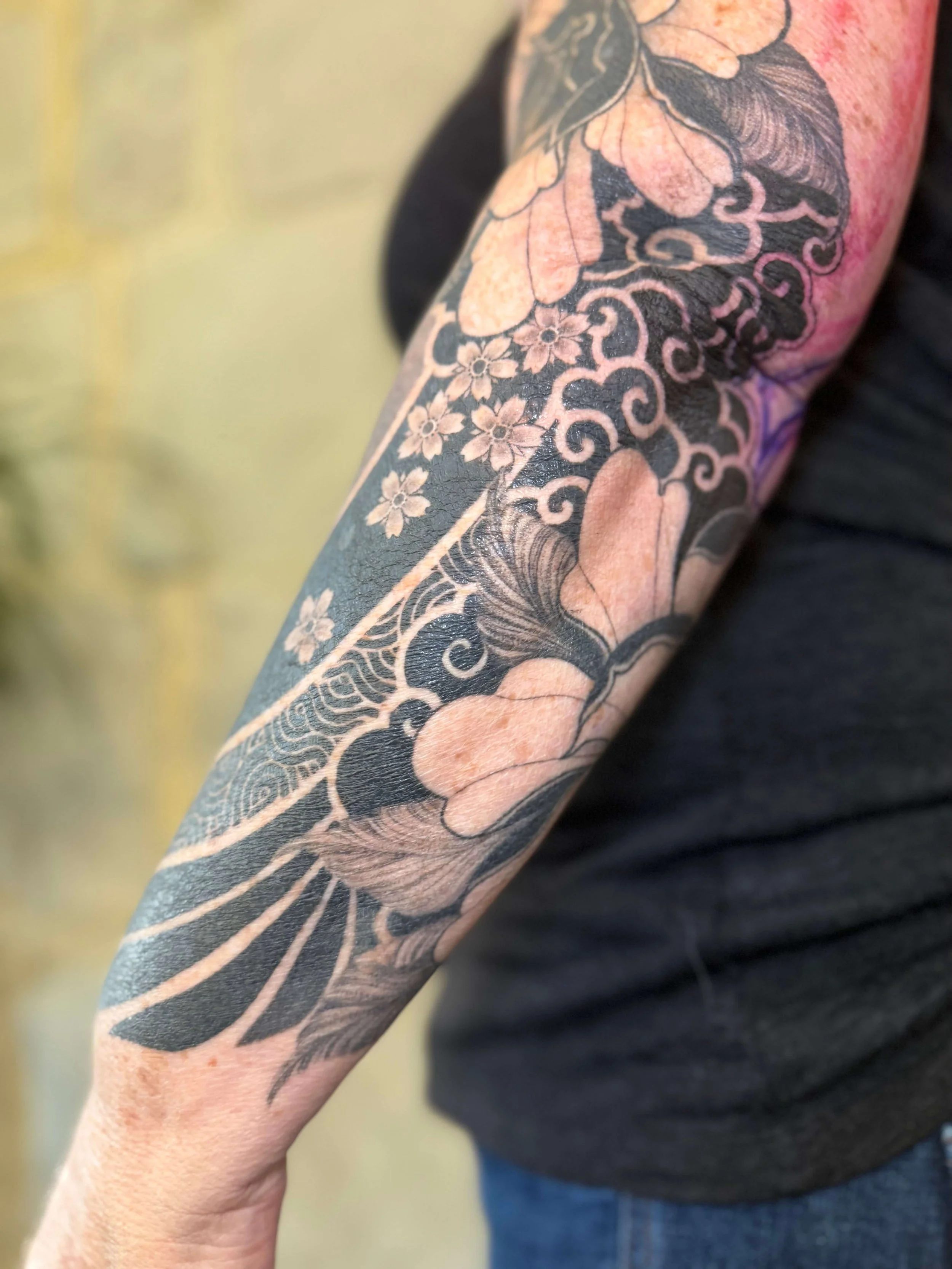 Close-up of a tattoo sleeve on a person's arm featuring black outline and beige shading, with floral and abstract patterns.