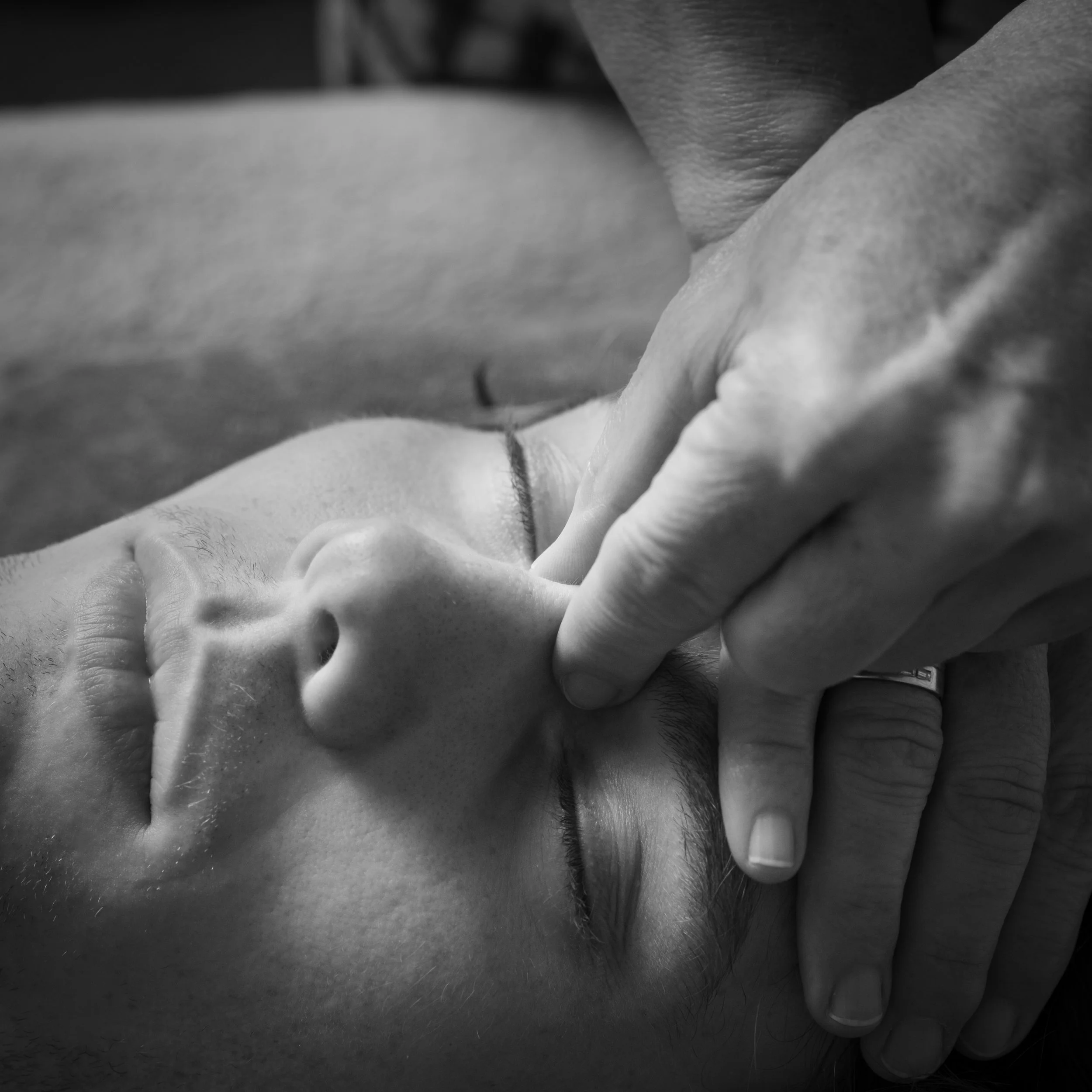 Close-up black and white photo of a women treating a mans face using craniosacral therapy