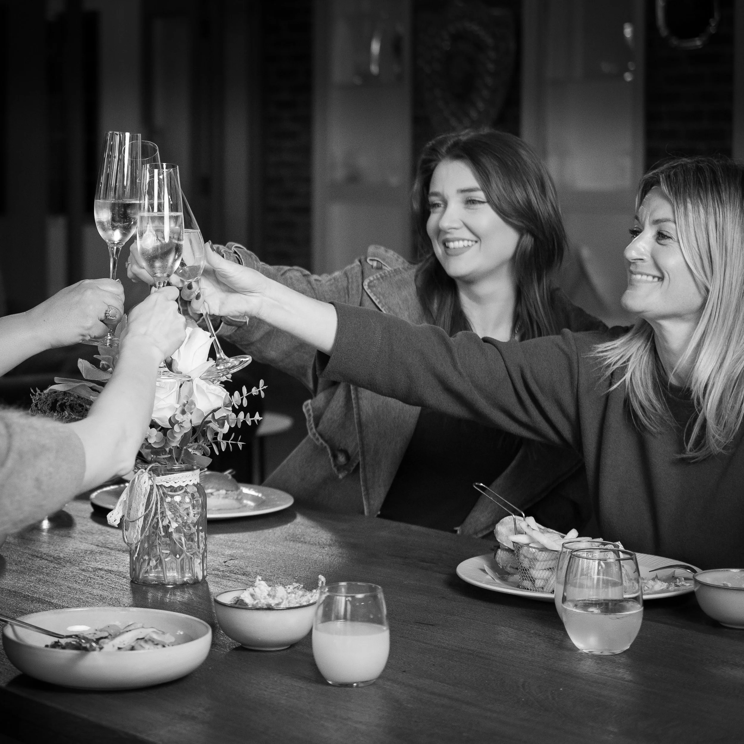 People raising glasses of champagne in a toast at a celebration or gathering, with a table of food and drinks in front of them.