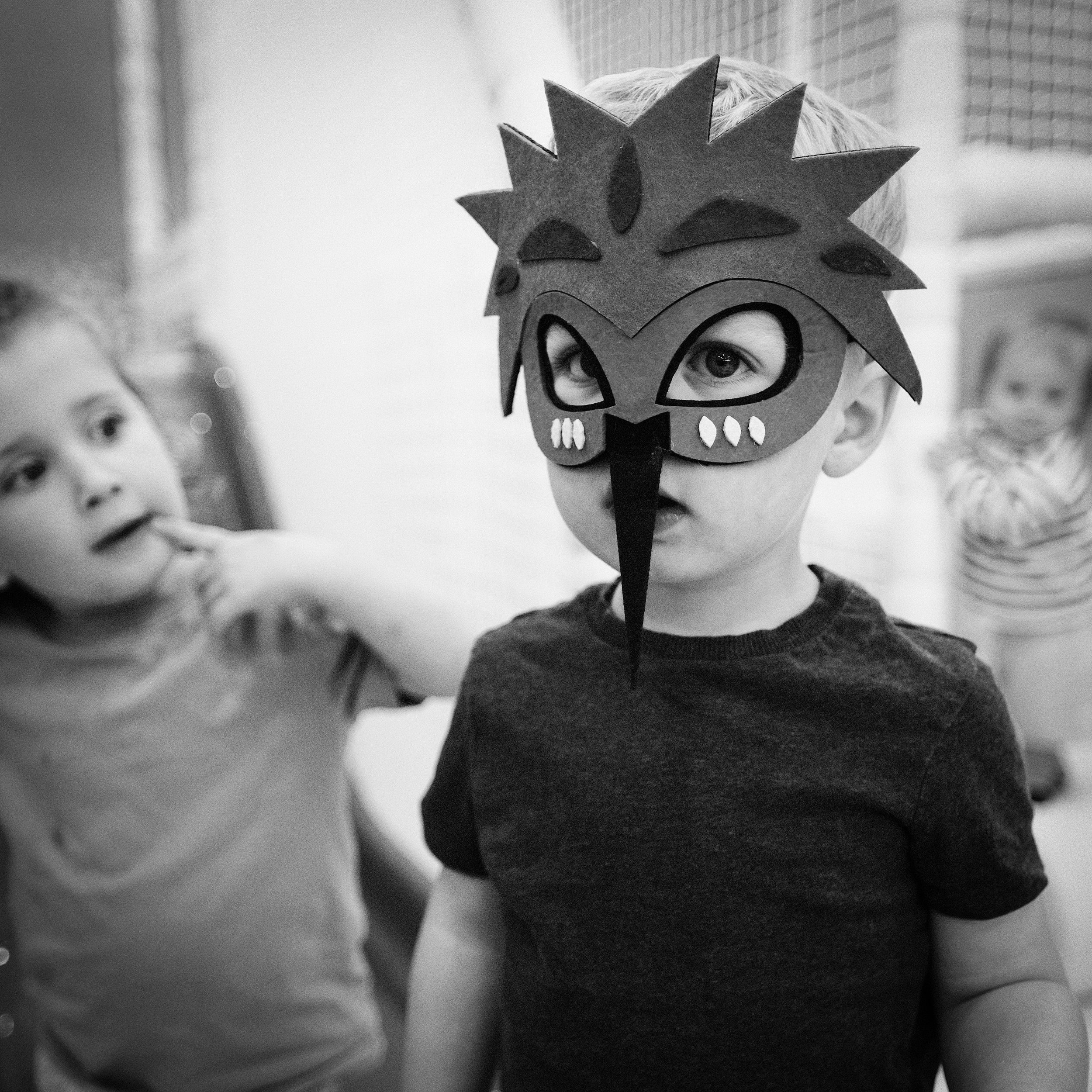 Child wearing a mask with decorative spikes, in black and white.