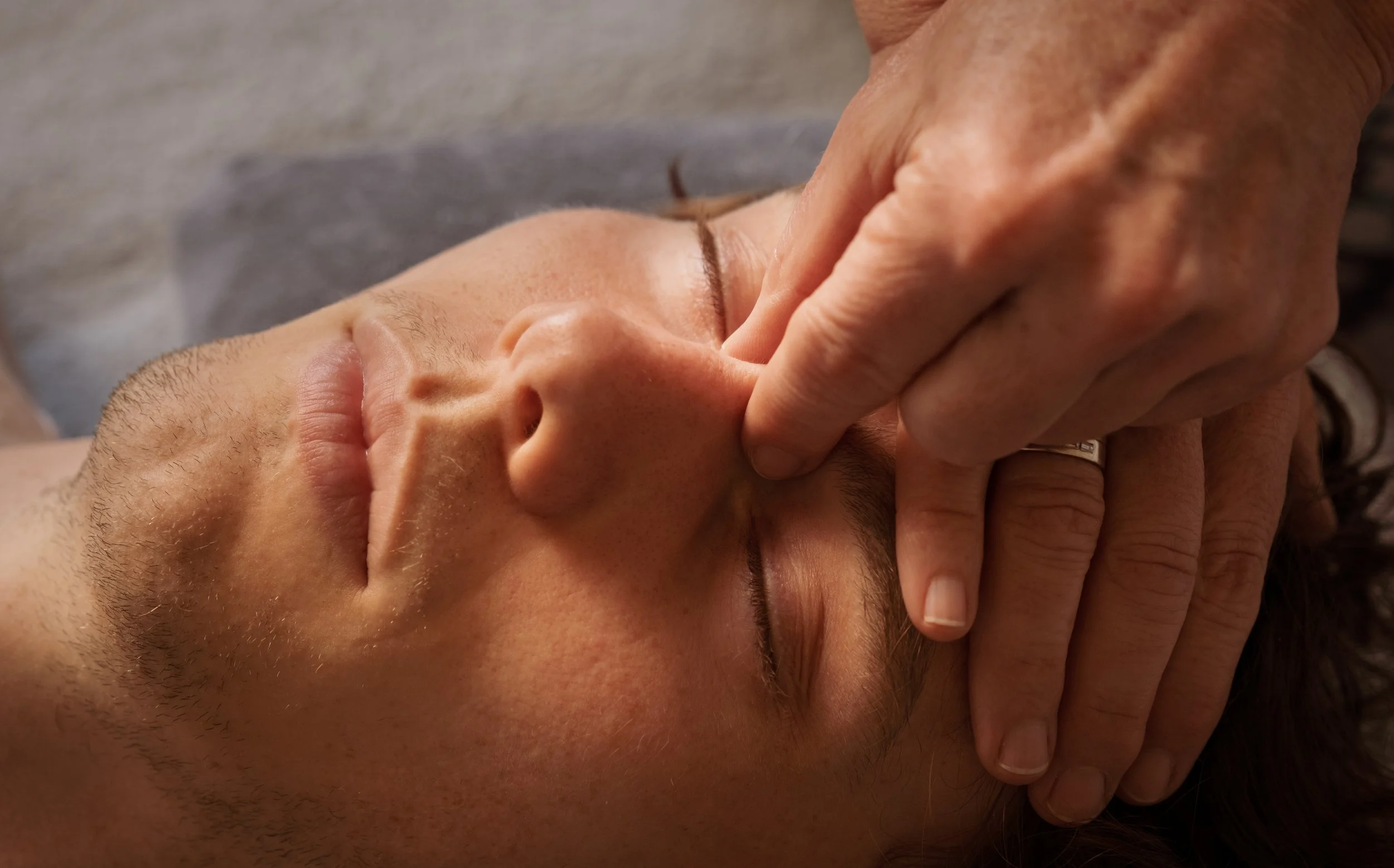 Person receiving a facial massage with a hand gently pressing on their cheek and chin.