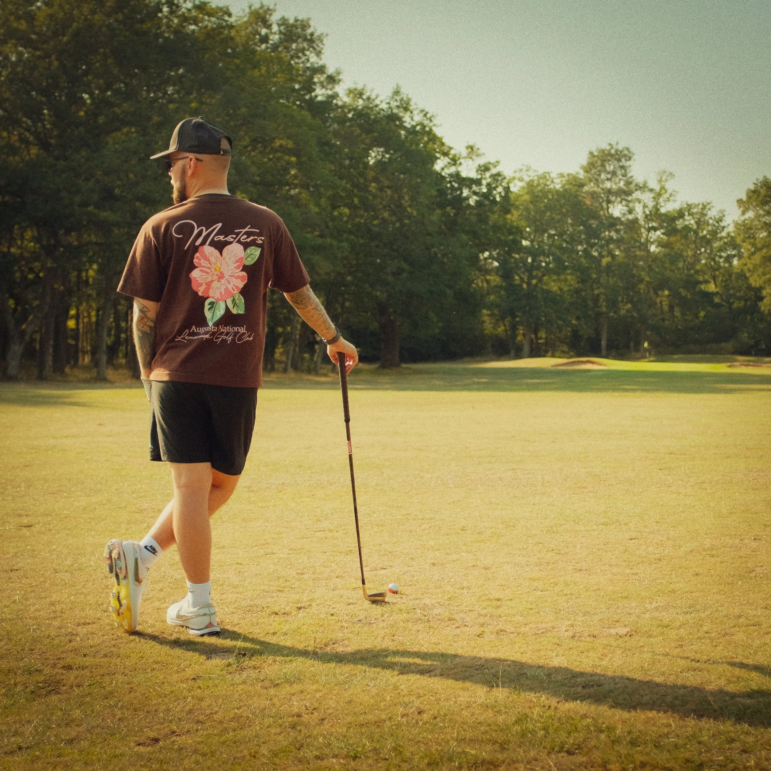A man is preparing to putt in a golf course during late afternoon or early evening, with trees and a slight hill in the background.