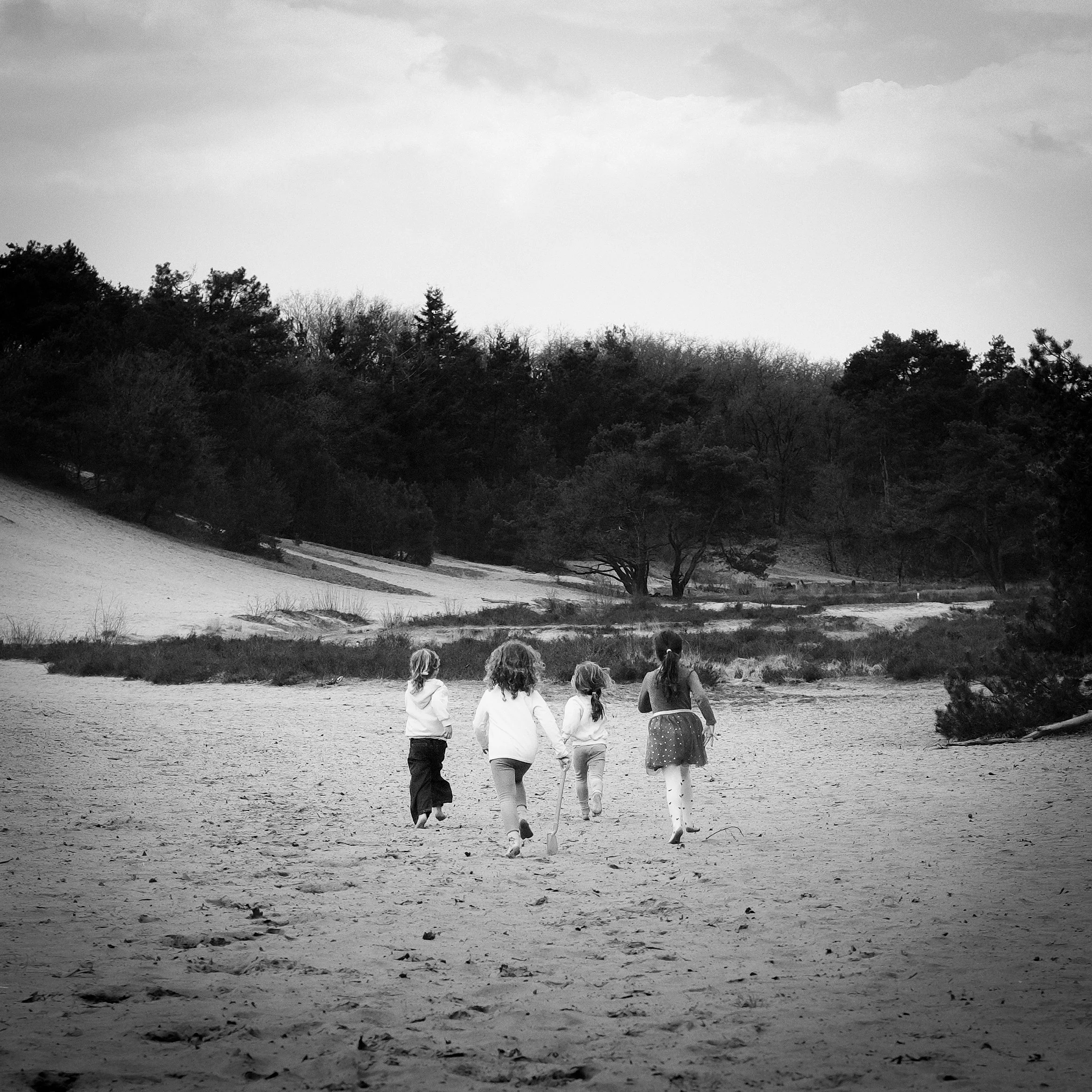 Five children walking on a sandy beach with trees in the background, in black and white.