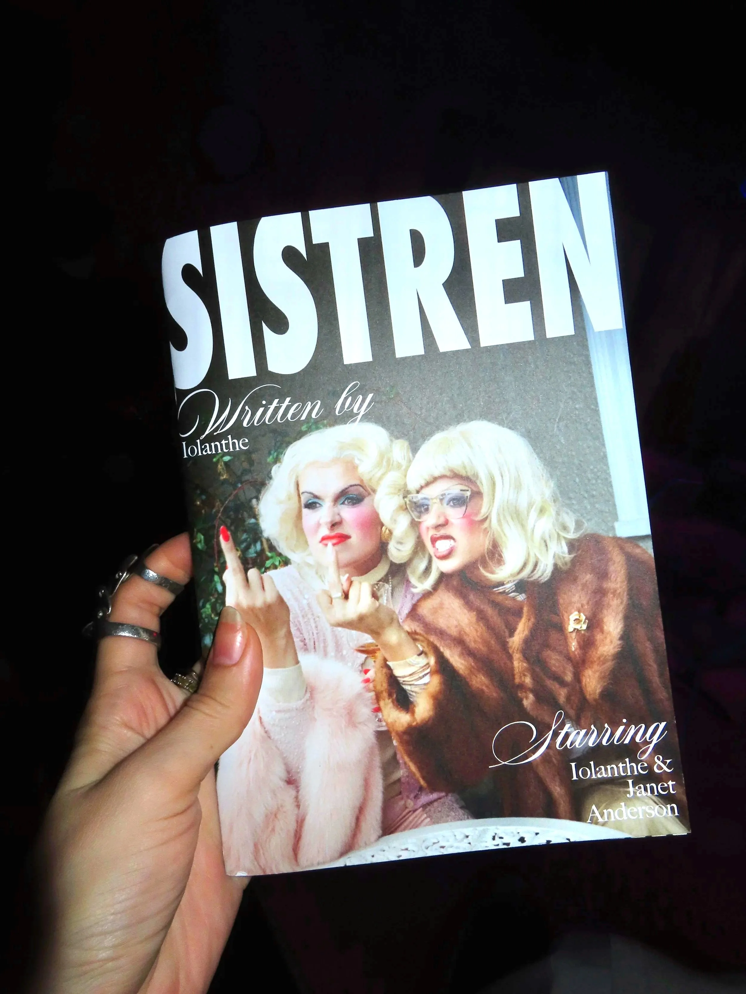 Book cover titled 'SISTER' written by Iolanthe, featuring two women with blonde hair dressed in vintage clothing, making expressive facial gestures.
