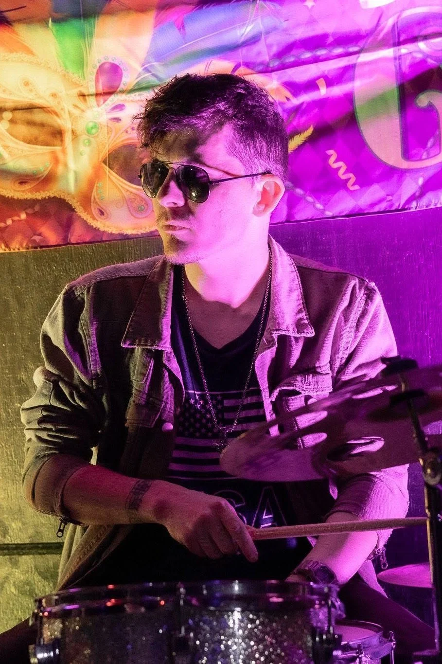Lost Street Records co-founder and music producer Ryandal Gilmore playing drums under purple and yellow stage lights during a live band performance.