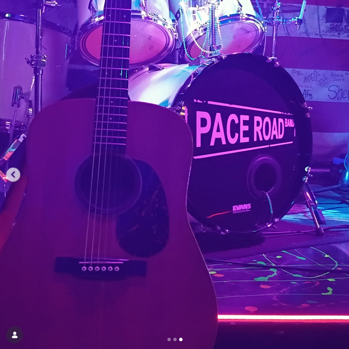 An acoustic guitar resting in front of a drum kit featuring the Pace Road Band logo.