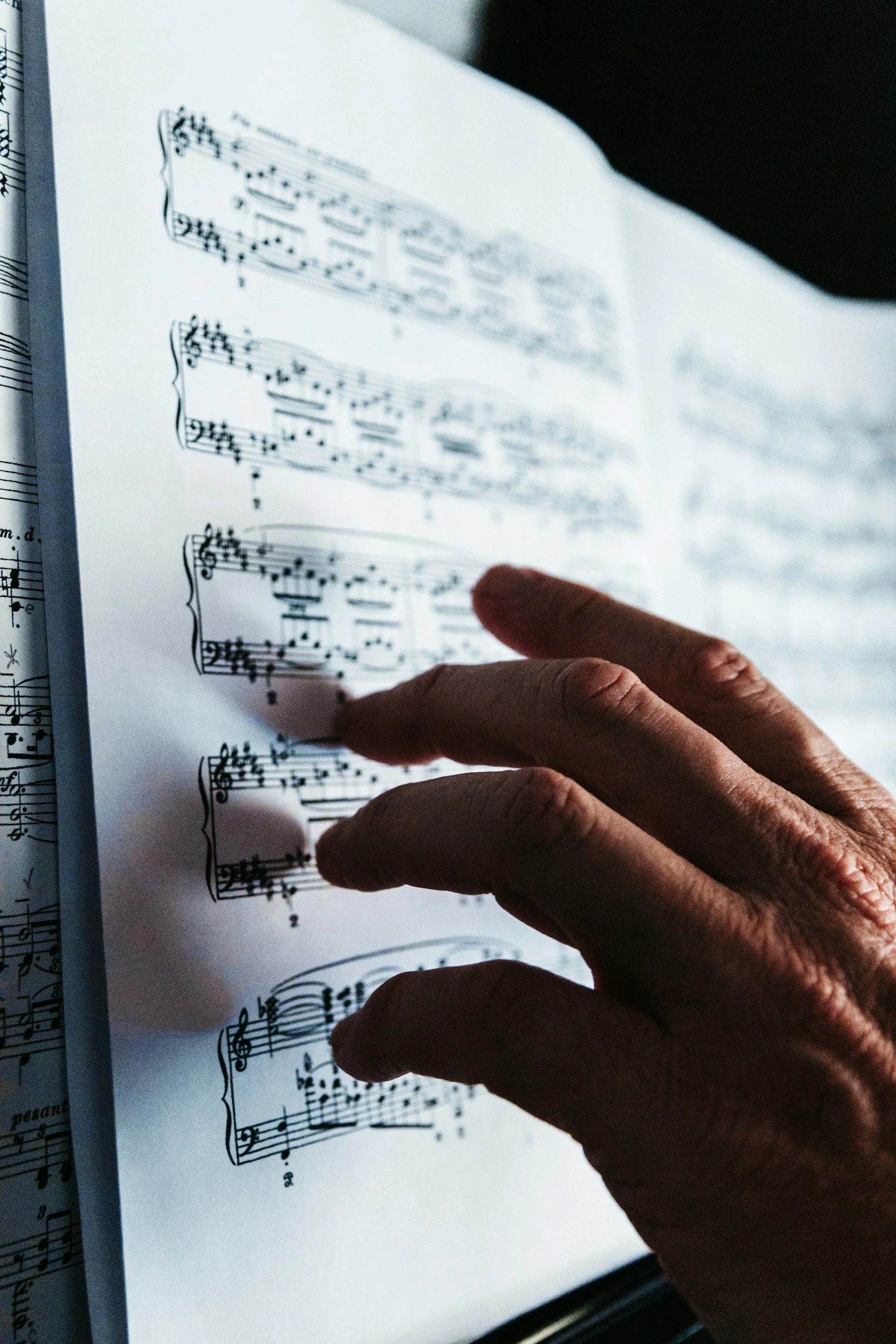 Close-up of an elderly person's hand touching sheet music in a music book.
