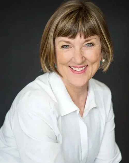 Portrait of a smiling woman with short brown hair wearing a white blouse against a dark background.