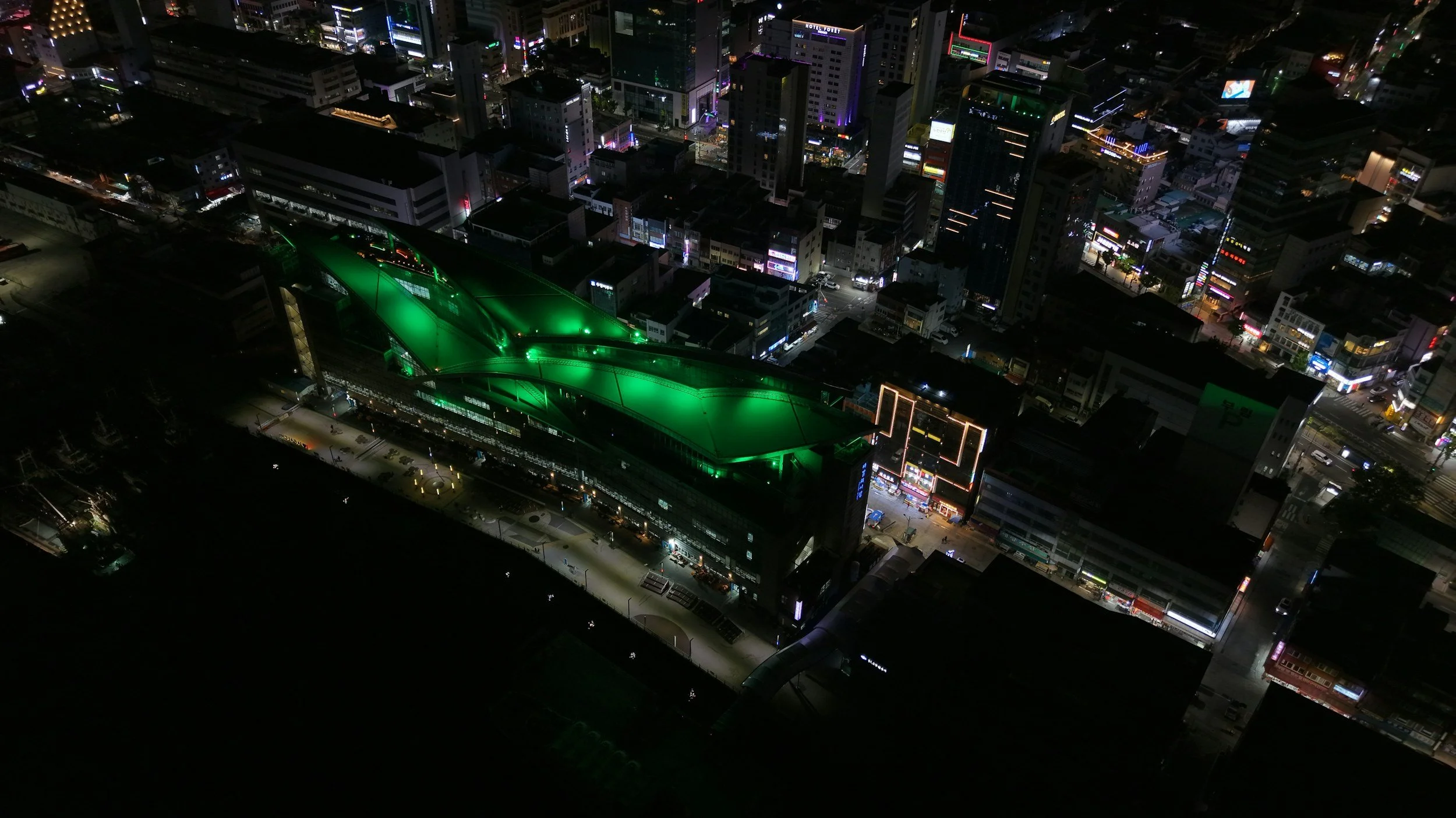Nighttime aerial view of a city with illuminated buildings, streets, and a distinctive green-roofed structure.