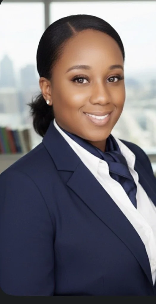Professional woman with dark hair tied back, wearing a navy blazer, white shirt, and navy scarf, smiling with a cityscape background.