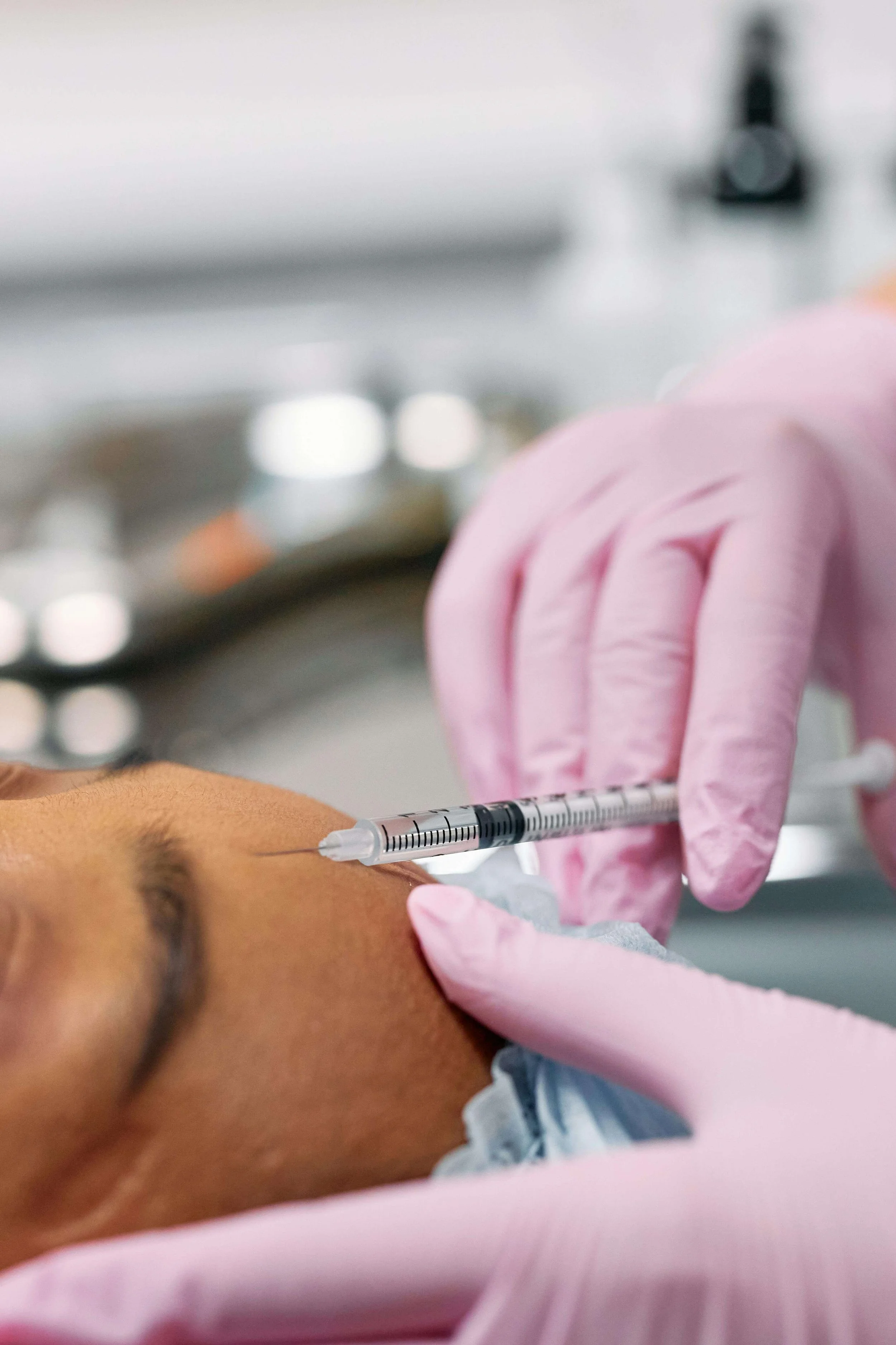 A person receiving Botox injection in their face from a healthcare professional wearing pink gloves