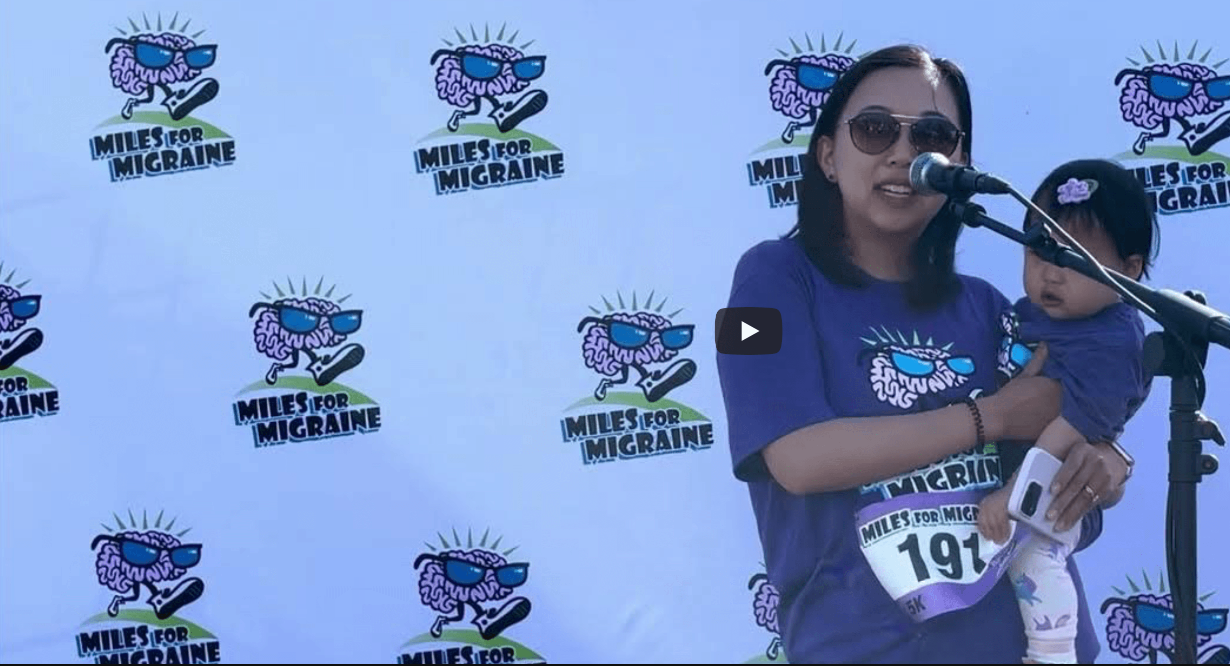 Doctor Nan Cheng wearing sunglasses and a purple shirt with the logo 'Miles for Migraine' is speaking into a microphone advocating for migraine disorders at Miles for migraine