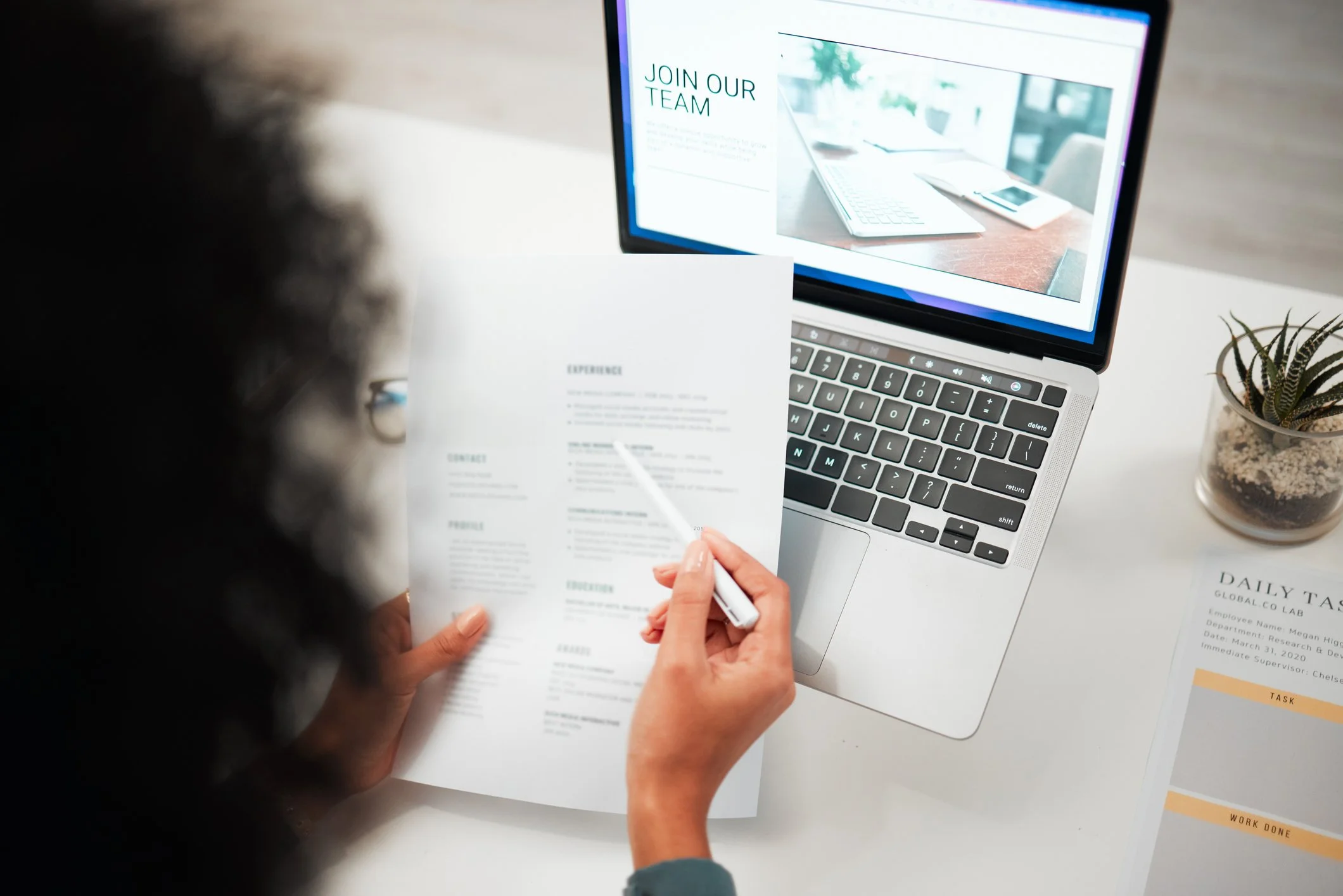 Medical administrator reviewing her resume at a desk with a laptop displaying a "Join Our Team" to work as a medical secretary