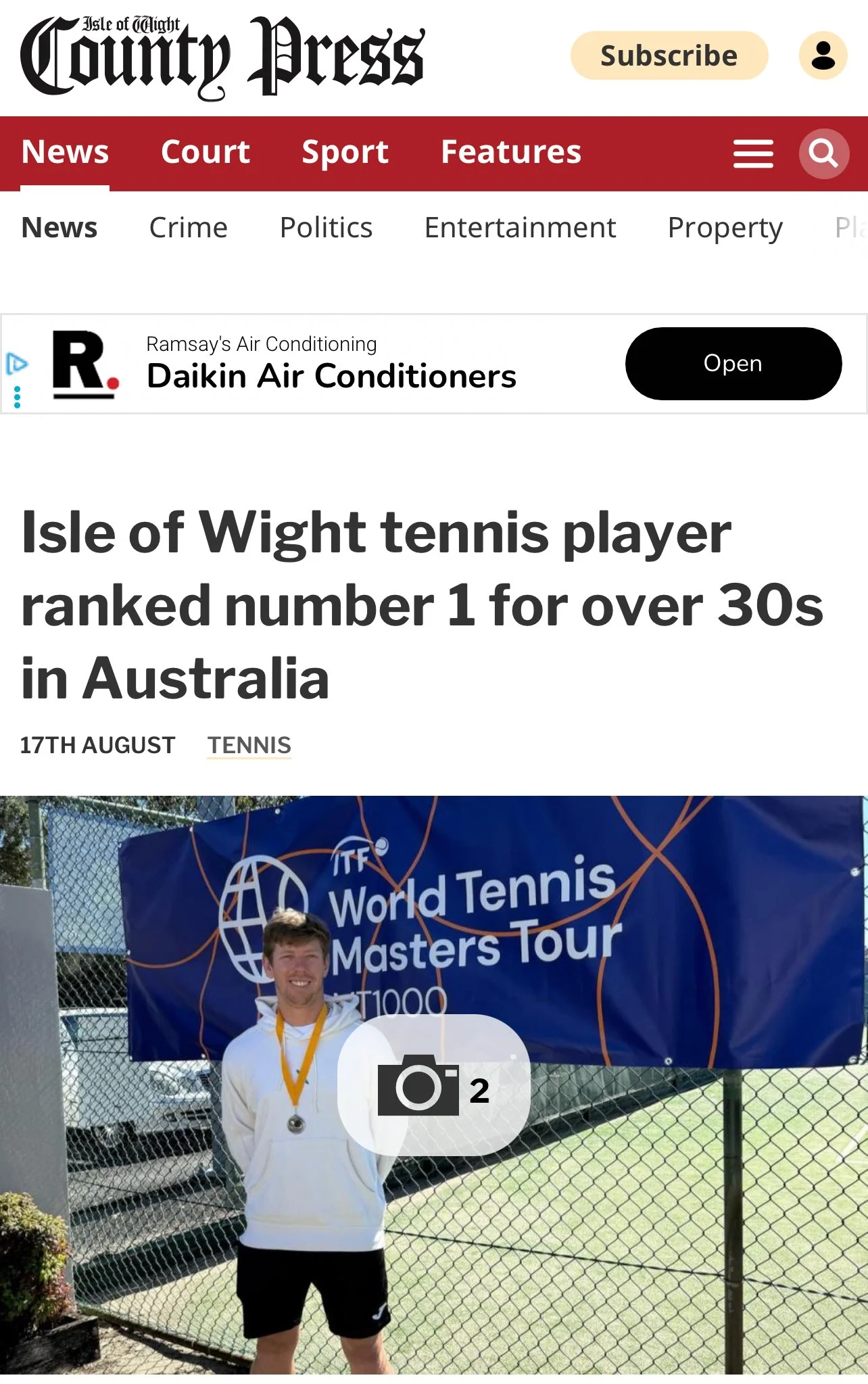 A man standing in front of a blue banner that reads 'ITF World Tennis Masters Tour' at an outdoor tennis court, wearing a white jacket, black shorts, and a medal around his neck.