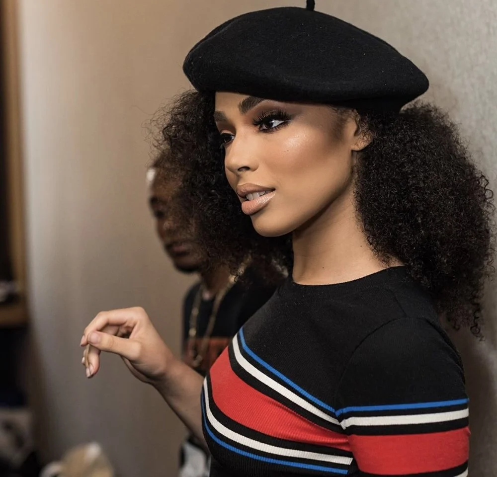 A woman with curly hair wearing a black beret and a black top with red, white, and blue stripes.