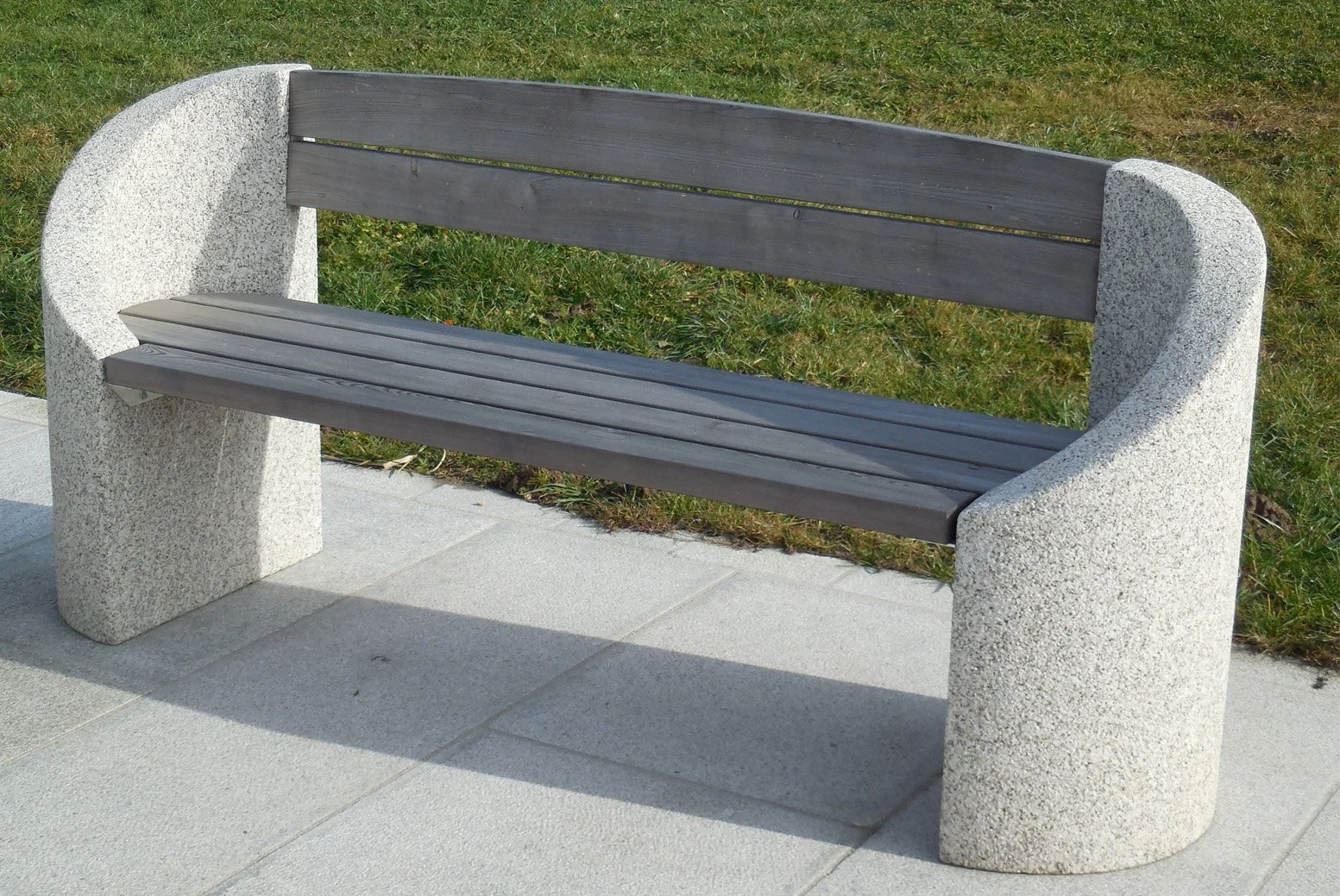 Bank aus Beton und Holz auf einem Gehweg mit Rasen im Hintergrund.