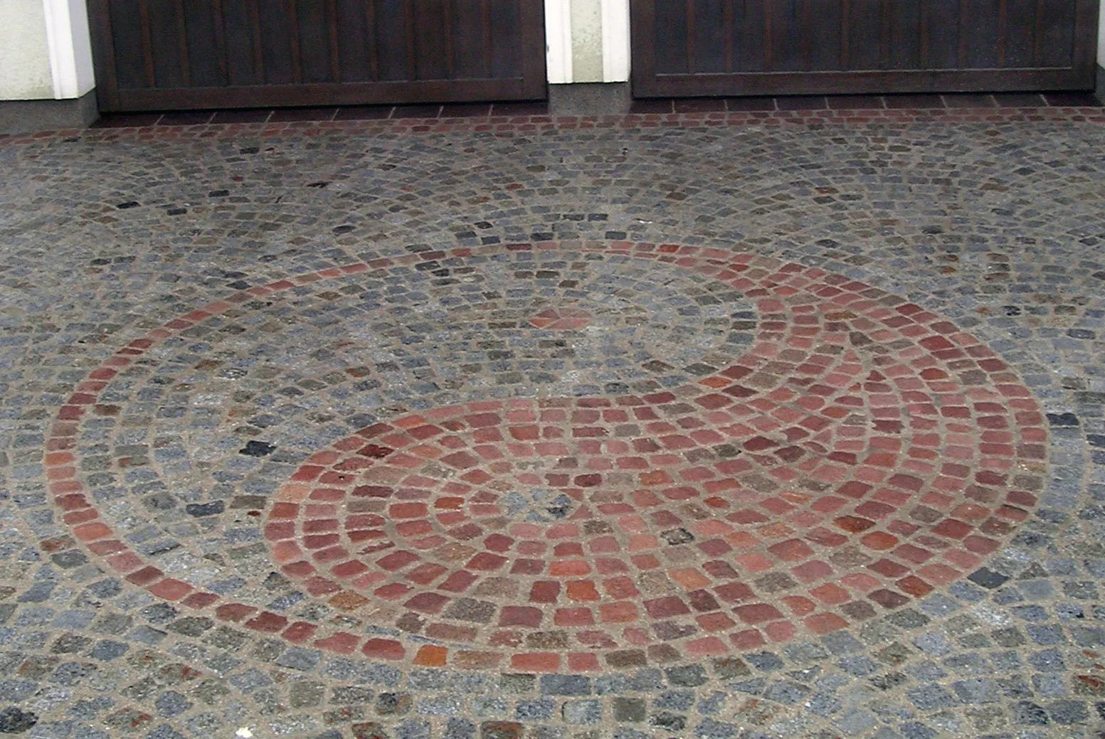 Verziertes Pflaster mit roten spiralförmigen Mustern vor einer doppelten Holztür