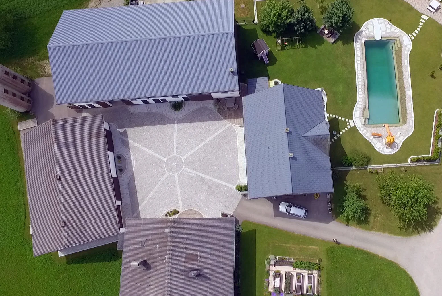 Luftaufnahme eines Hauses mit Garten, Pool, Spielplatz und Zufahrtsweg