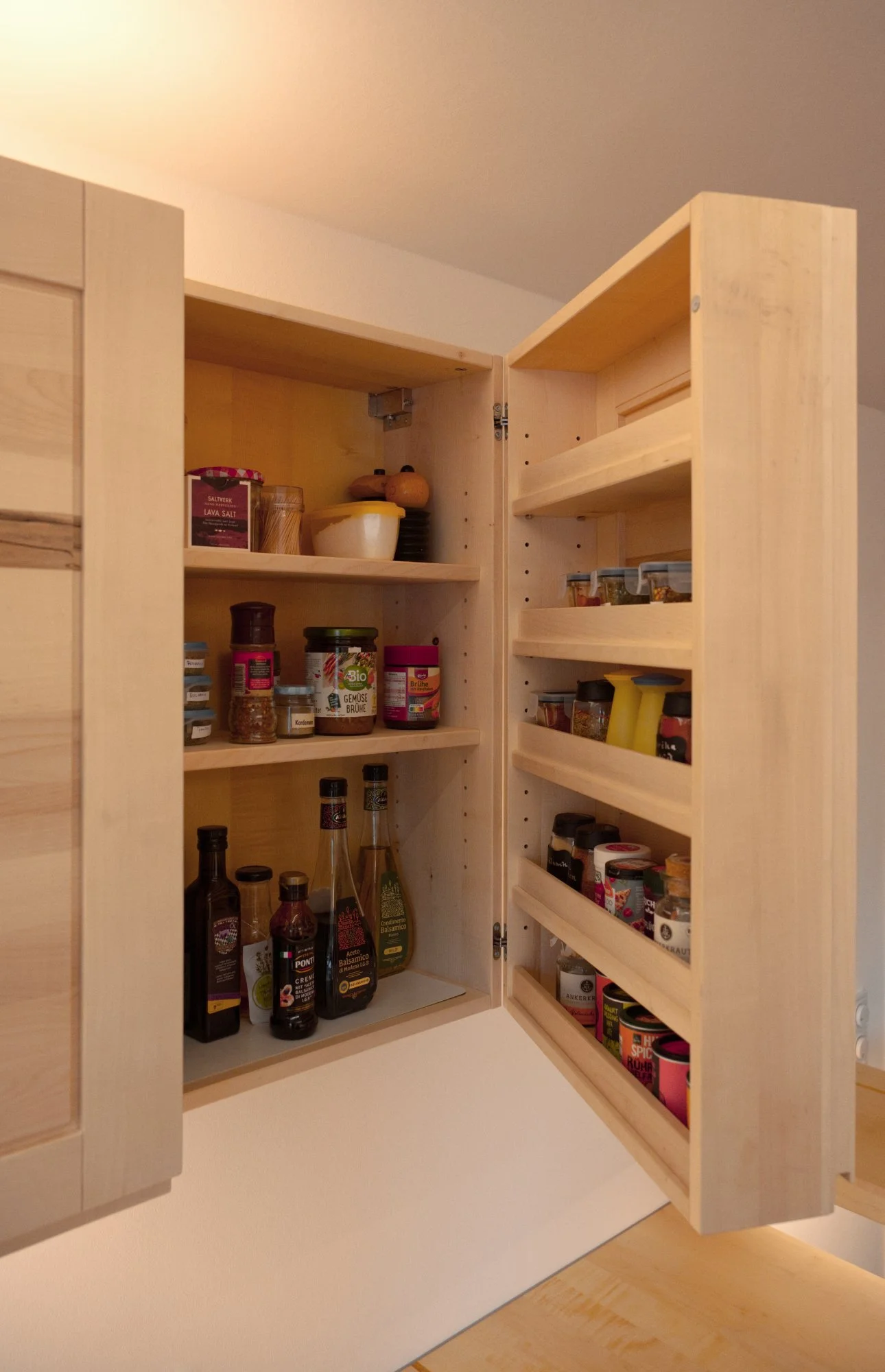 Ein offener Holzwand-Küchenschrank mit verschiedenen Gewürzen, Flüssigkeiten und Lebensmitteln darin.