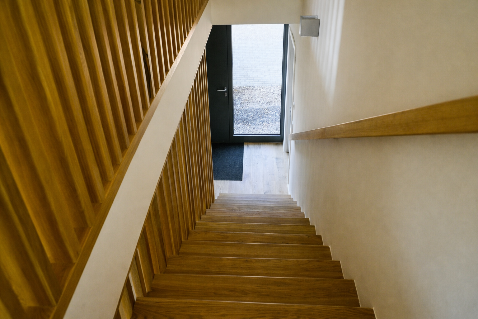 Innenaufnahme einer Treppe aus Holz, Blick nach unten zur Haustür mit Glasfront, Flur mit Fußmatte.
