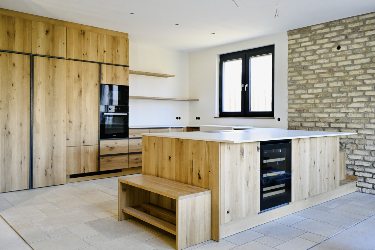 Moderne Küche mit Holz-Schrankmöbeln, einem schwarzen Fenster, einem Backofen und einem Wein-Kühlschrank in einem offenen Raum.