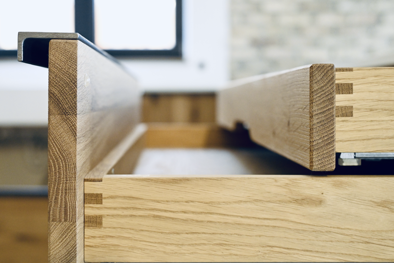 Nahaufnahme von einem Holzschubkasten mit sichtbaren Fingerzinkenverbindungen, im Hintergrund eine Fensterfront.