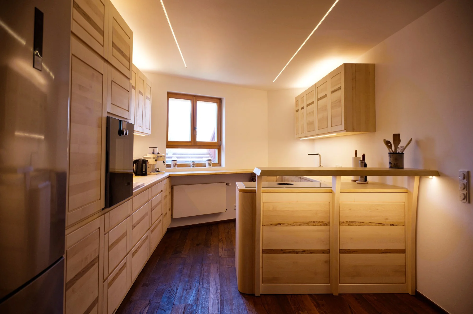 Moderne Küche mit Holzschränken, Holzarbeitsflächen, einem Fenster, eingebautem Herd und Küchenutensilien auf der Arbeitsplatte, warme Beleuchtung.