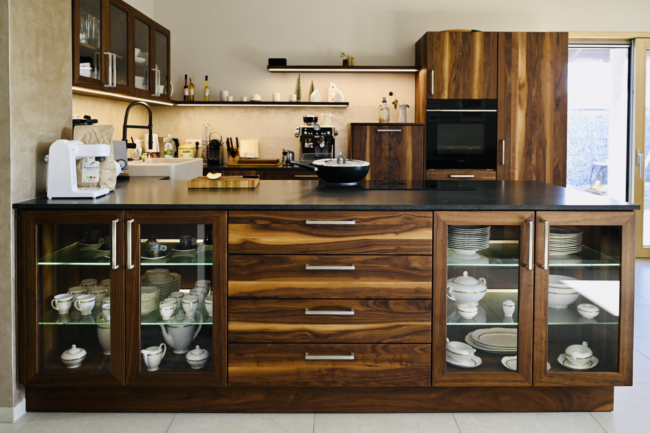 Eine moderne Küche mit Holzschränken, einem schwarzen Küchenarbeitsplatte, Geschirr im Glaskasten und Küchengeräten.