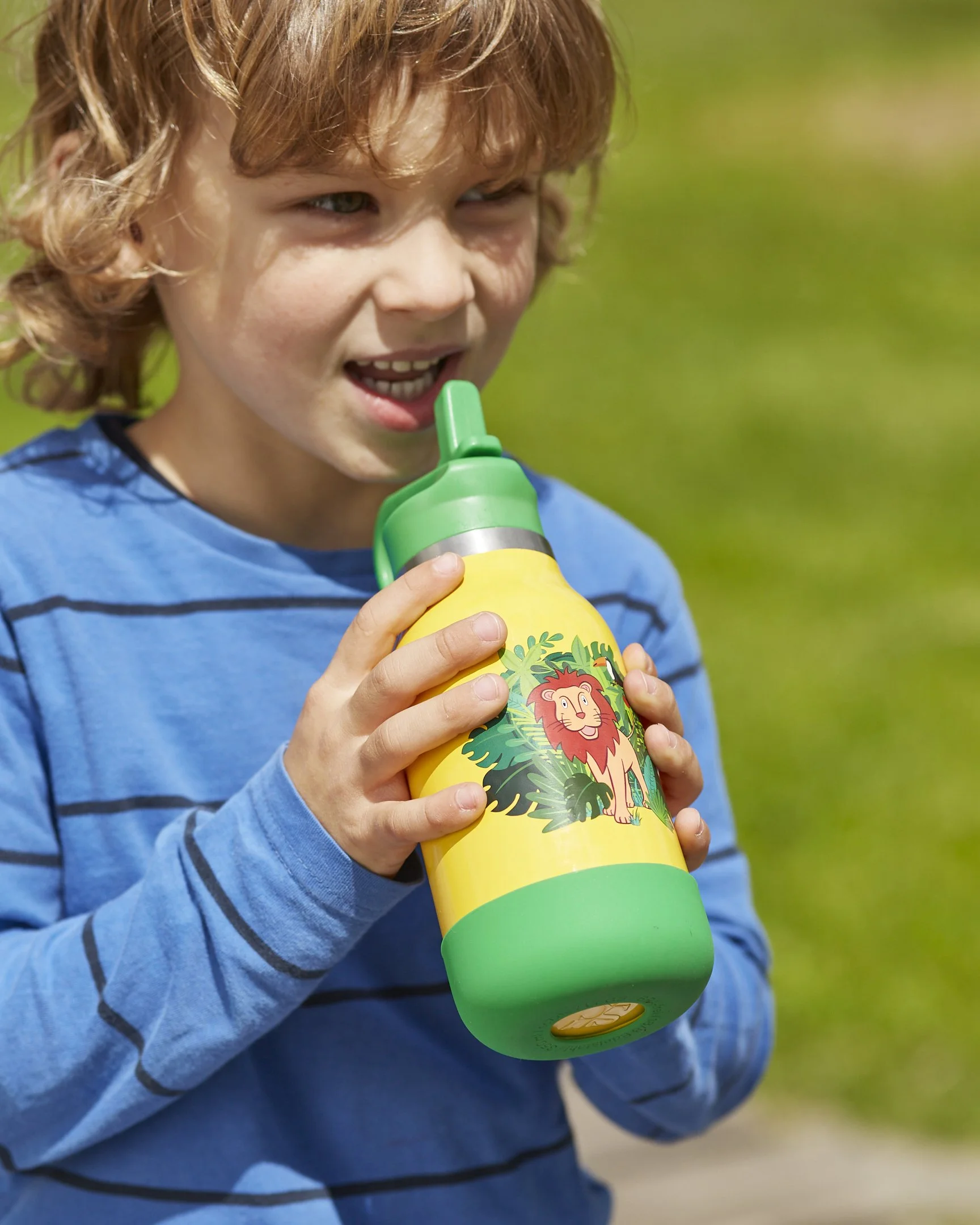 Junge mit braunen, lockigen Haaren trinkt aus einer bunten Trinkflasche mit Löwengrafik
