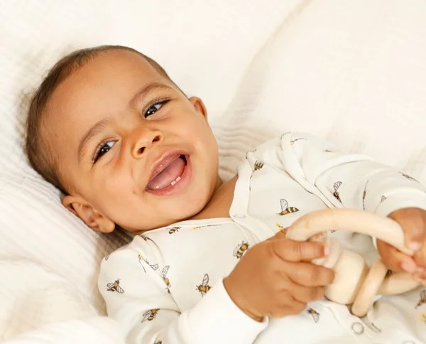Lächelnder kleiner Junge in weißen Pyjama mit Bienenmuster, liegend auf einem weißen Bett, hält ein Spielzeug.