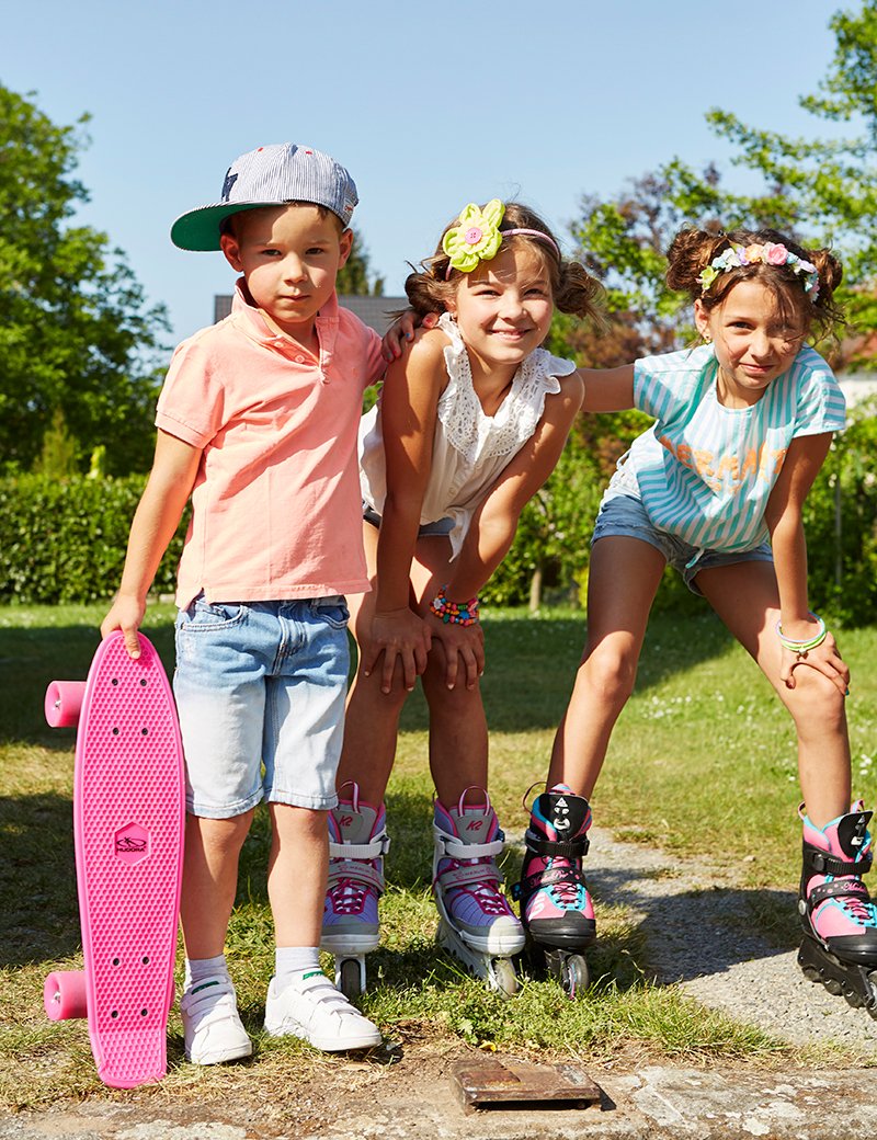 Drei Kinder in bunten Sommerlooks mit Inlineskates, Skateboard und Headphones – Kinderfotografie im Editorial- und Lifestyle-Stil