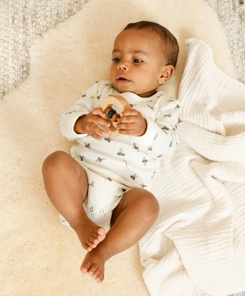 Kleines Baby liegt auf einer weichen Decke und hält ein Spielzeug in den Händen, während es entspannt aussieht.