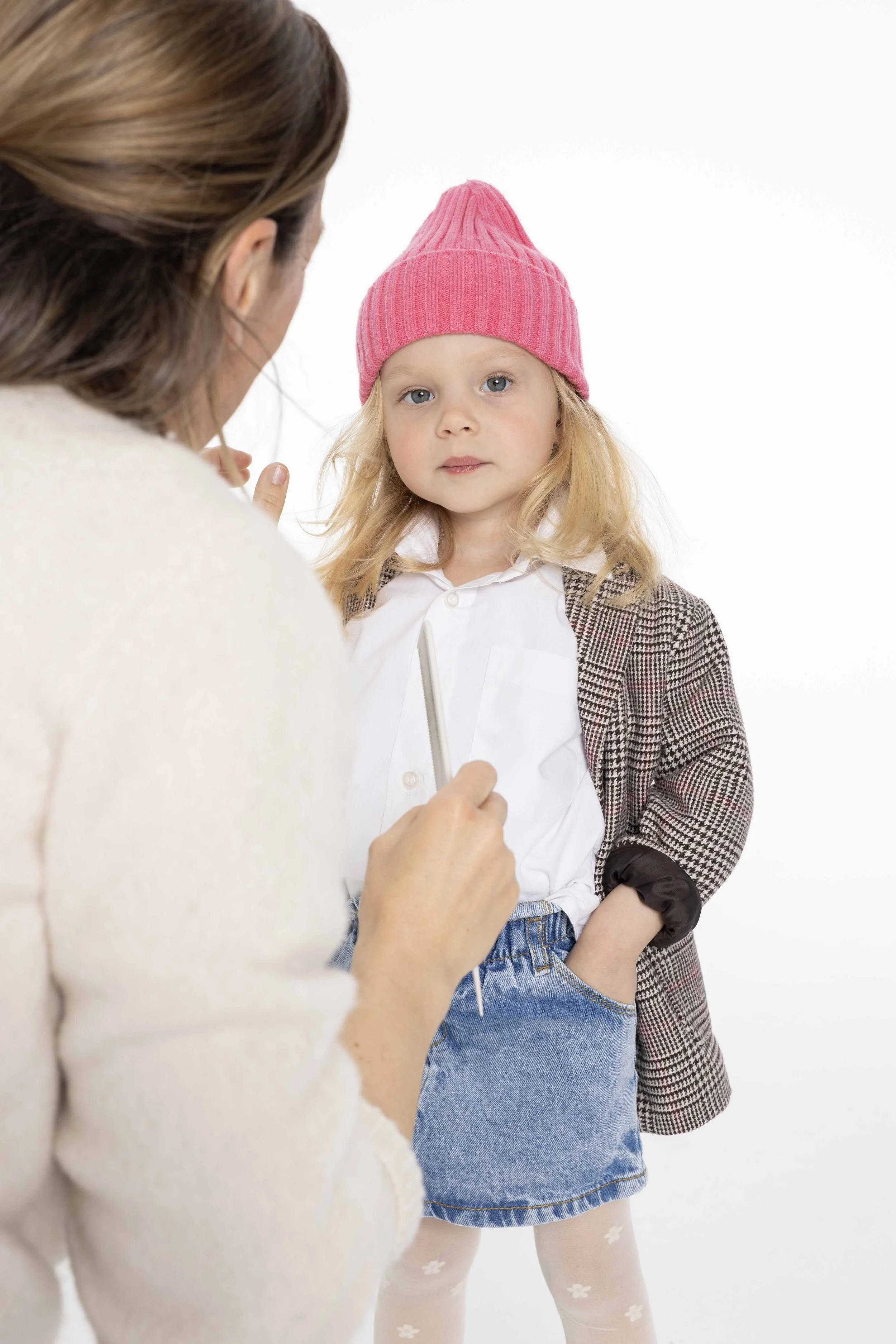 Mädchen vor weißem Hintergrund, wird von einer Frau zurecht gemacht und trägt einen Jeansroch und pinkne Mütze.