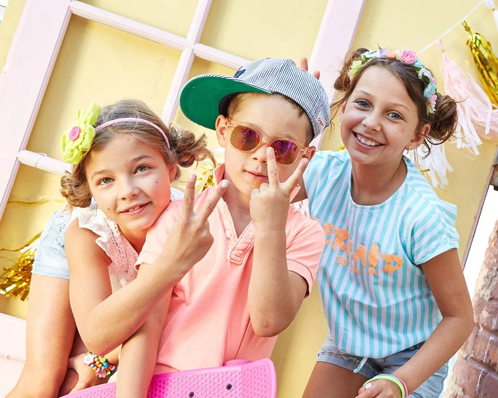 Drei Kinder feiern eine Party mit bunten Dekorationen im Hintergrund.