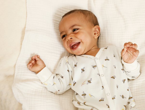 Lächelnder kleiner Junge liegt auf einem weißen Kissen und trägt einen weißen Schlafanzug mit Bienenmuster.