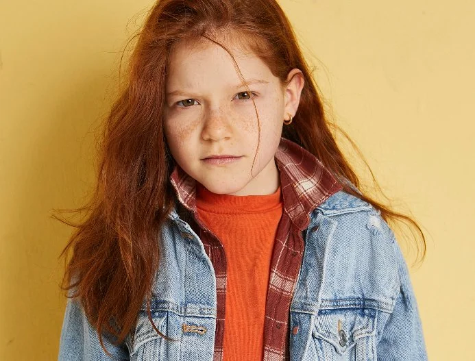 Rothaariges Mädchen in Denim-Layering-Look vor gelber Studio-Wand – moderne Kinderfotografie mit Bewegung und Ausdruck