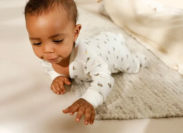 Kleines Baby liegt auf dem Bauch auf einem Teppich und greift nach etwas.