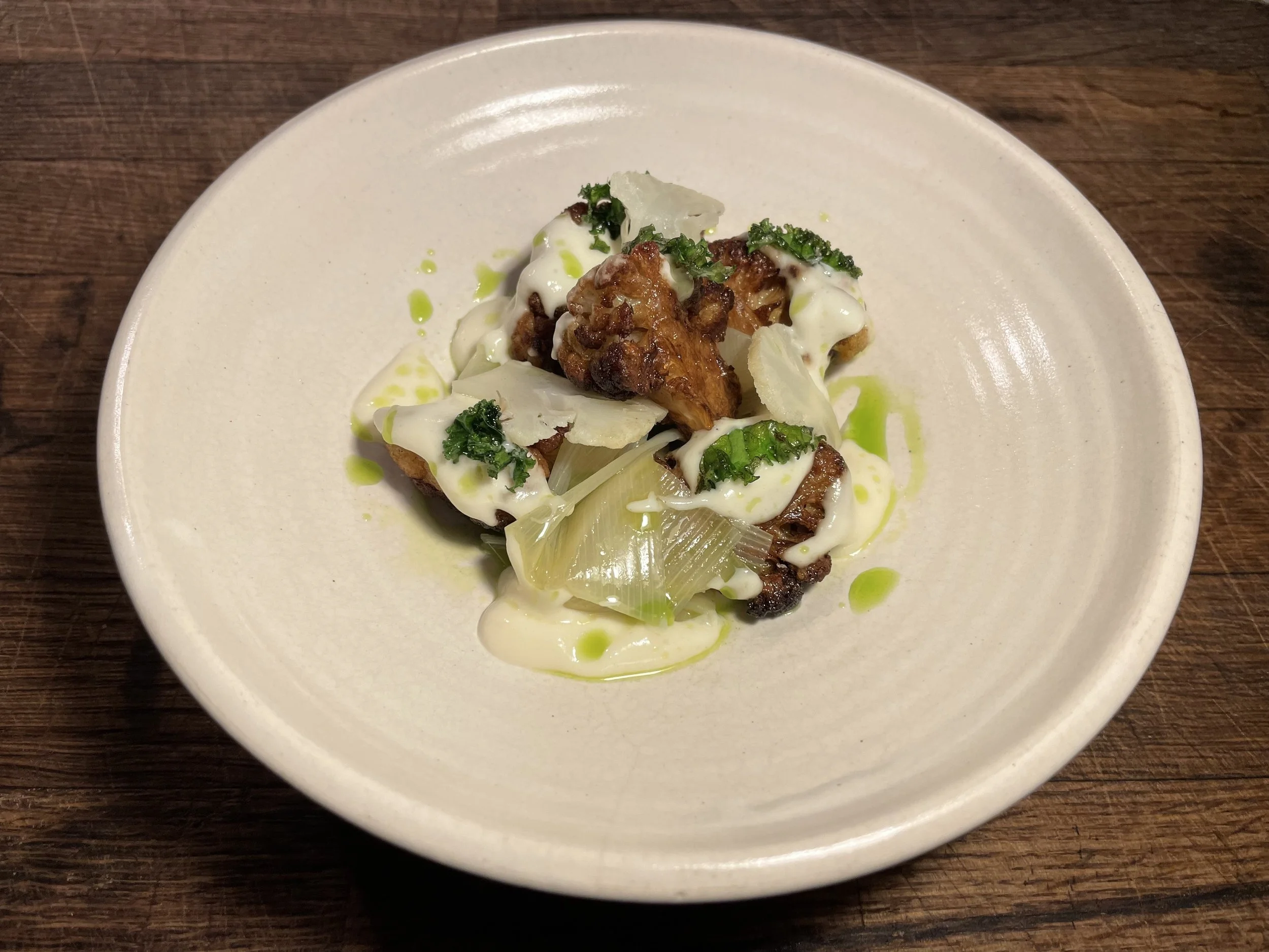 Gourmet dish with fried meat, creamy sauce, and green herbs on a white plate.