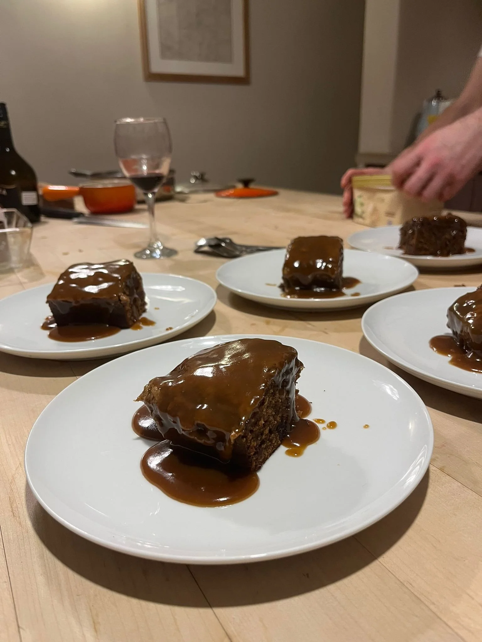 Four plates with slices of chocolate cake topped with caramel sauce on a dining table.