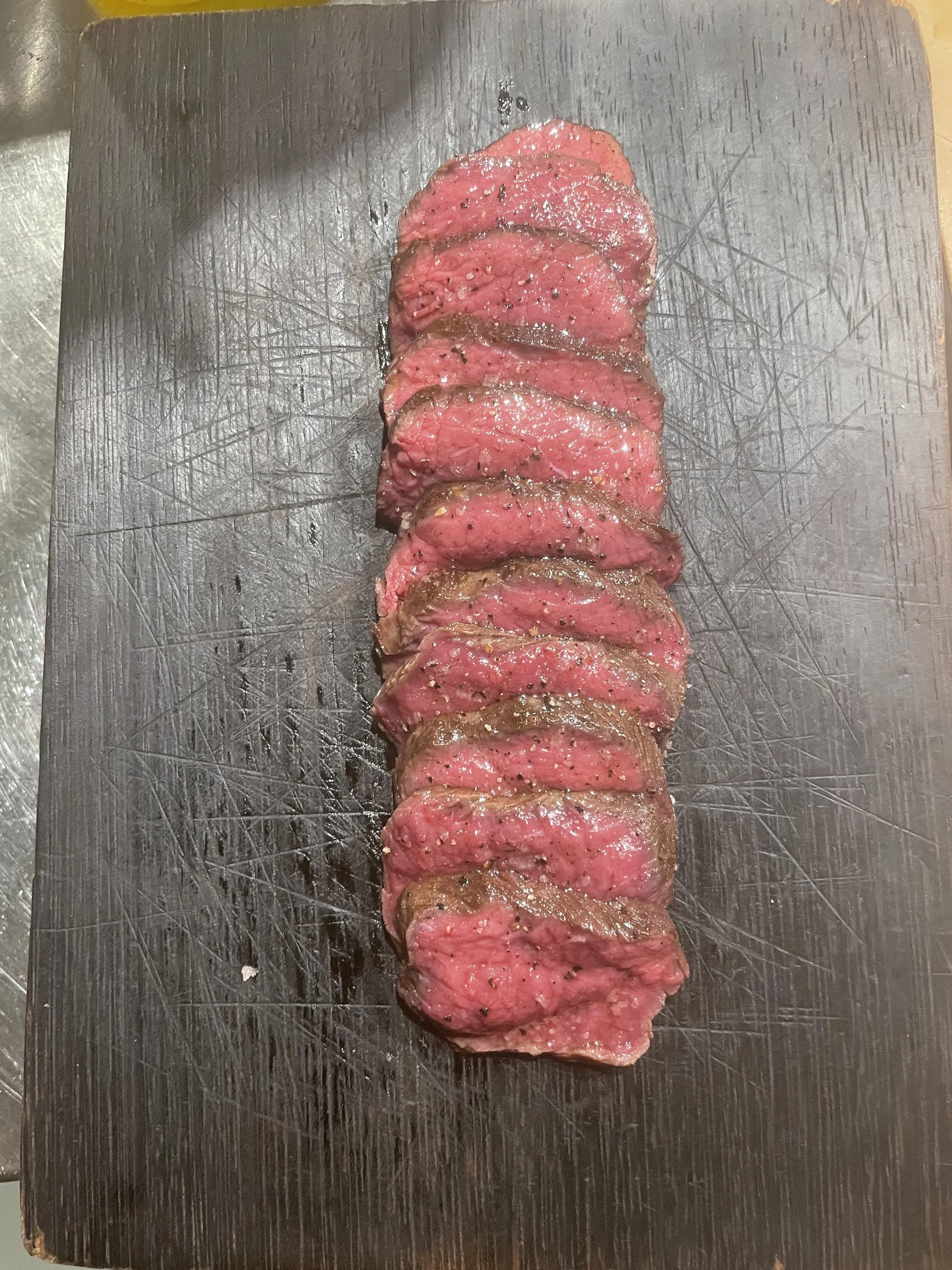 Sliced cured meat, possibly steak, on a black cutting board.