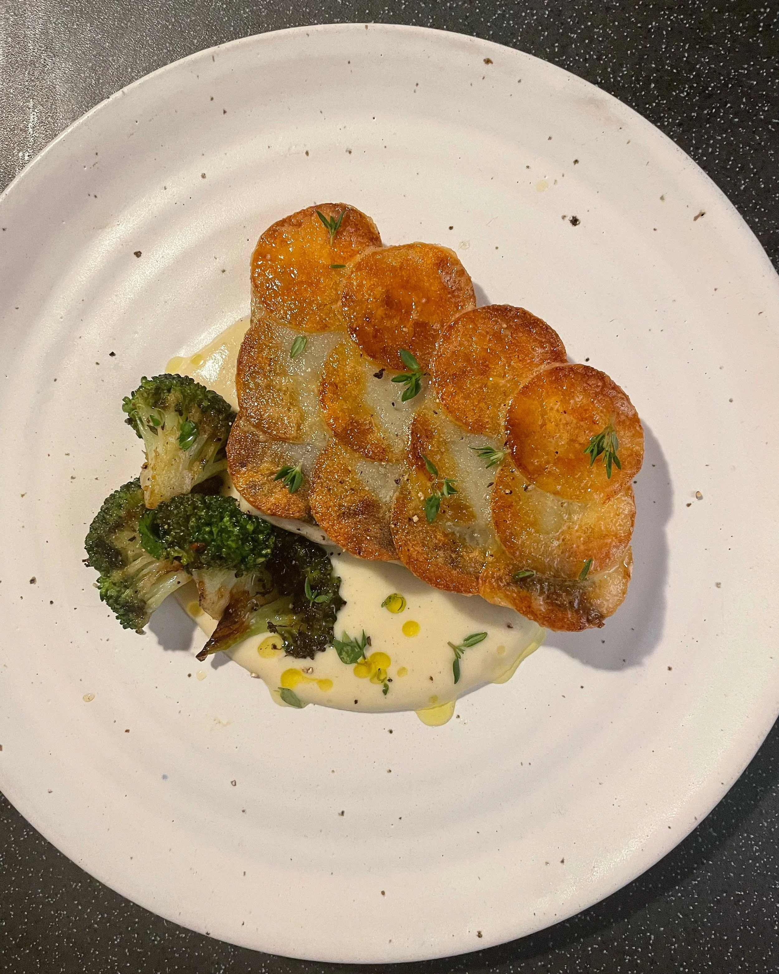 Plate with roasted broccoli and potato scaled sea bass, garnished with celeriac hollandaise and herbs.