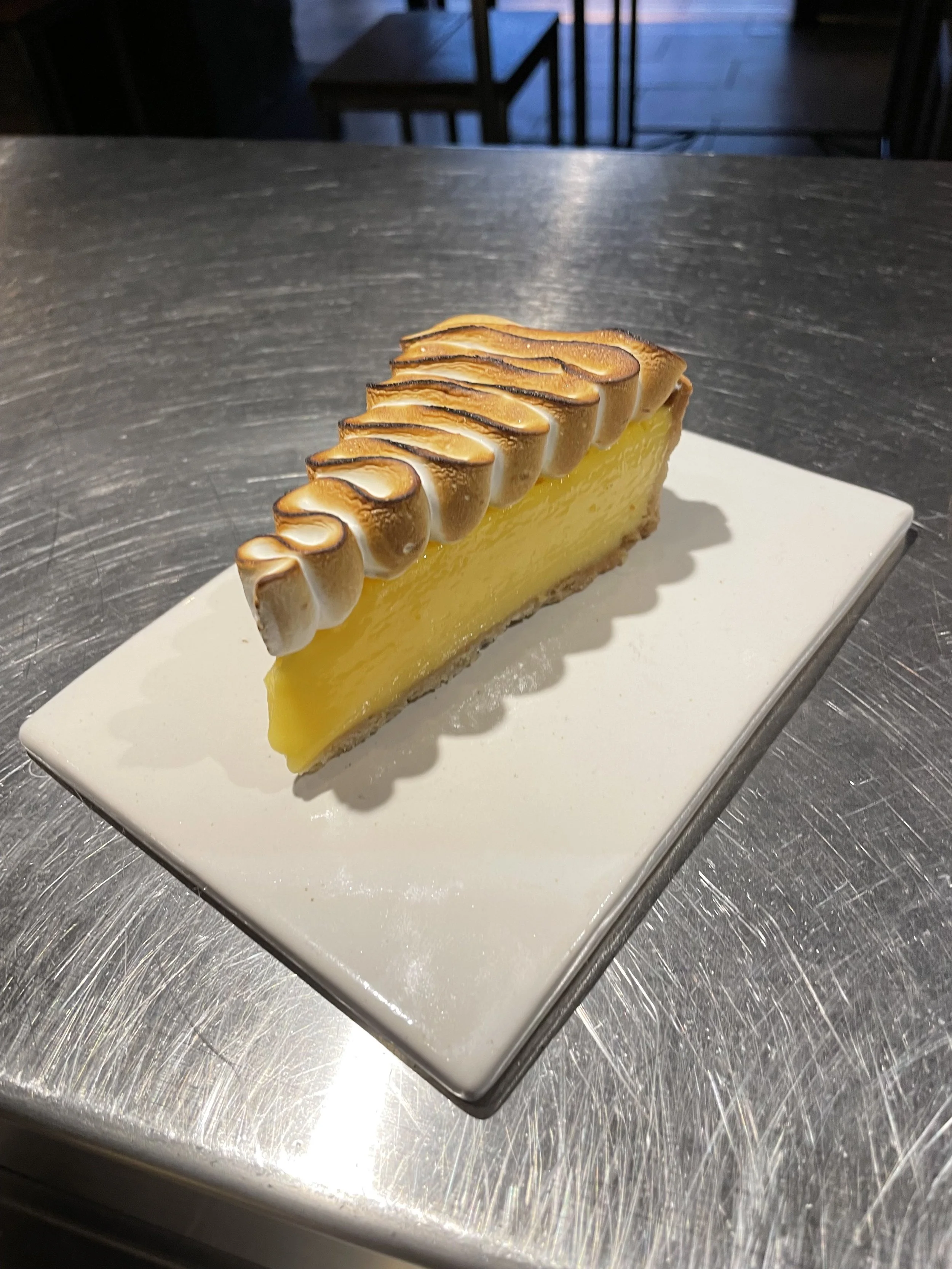 Slice of lemon meringue tart with toasted meringue topping on a white rectangular plate