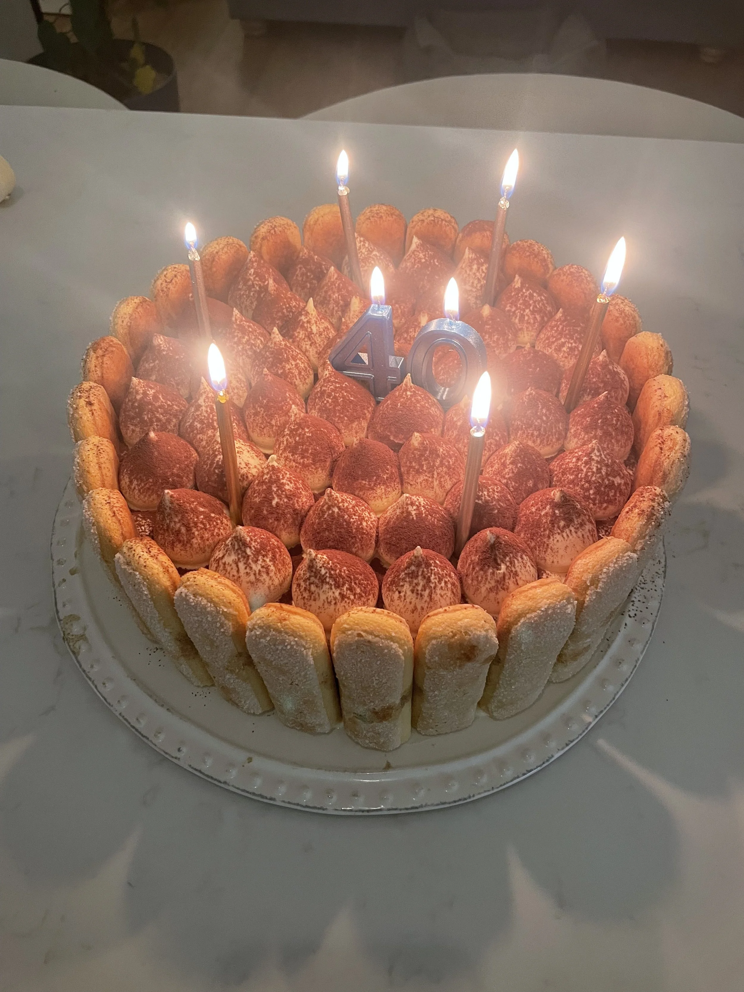 A birthday cake with lit candles and a blue "40" birthday number in the center.