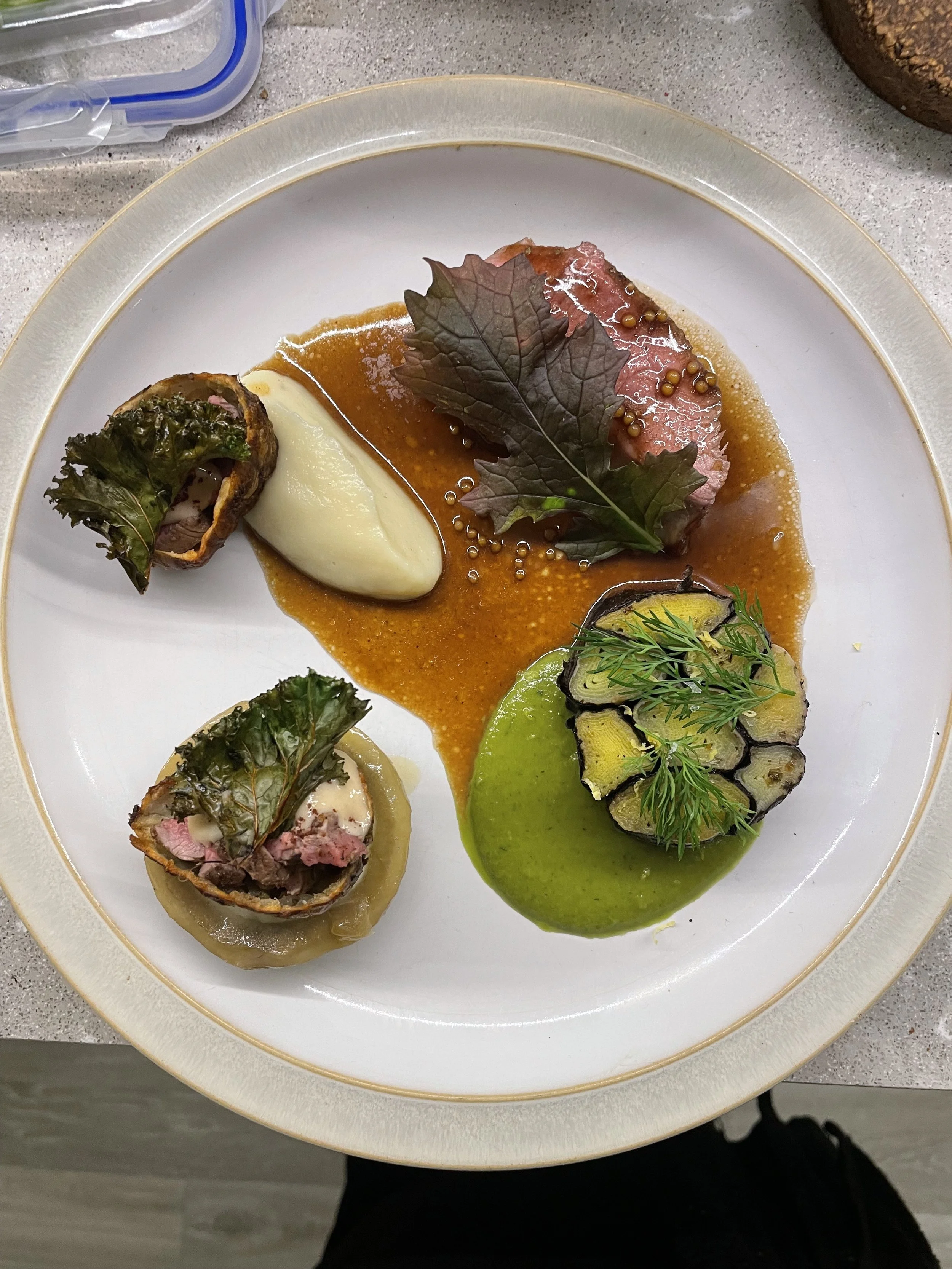 A gourmet plate with serving of fine beef, mashed potatoes, roasted vegetables, colorful sauces, and garnishes.