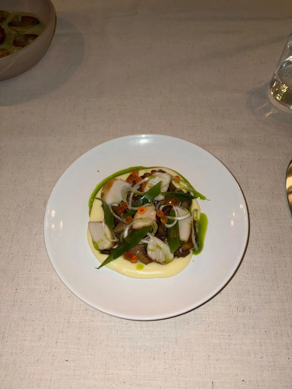 A plated dish with a creamy yellow puree, topped with sautéed mixed vegetables, green onions, red pepper flakes, and a drizzle of green sauce.