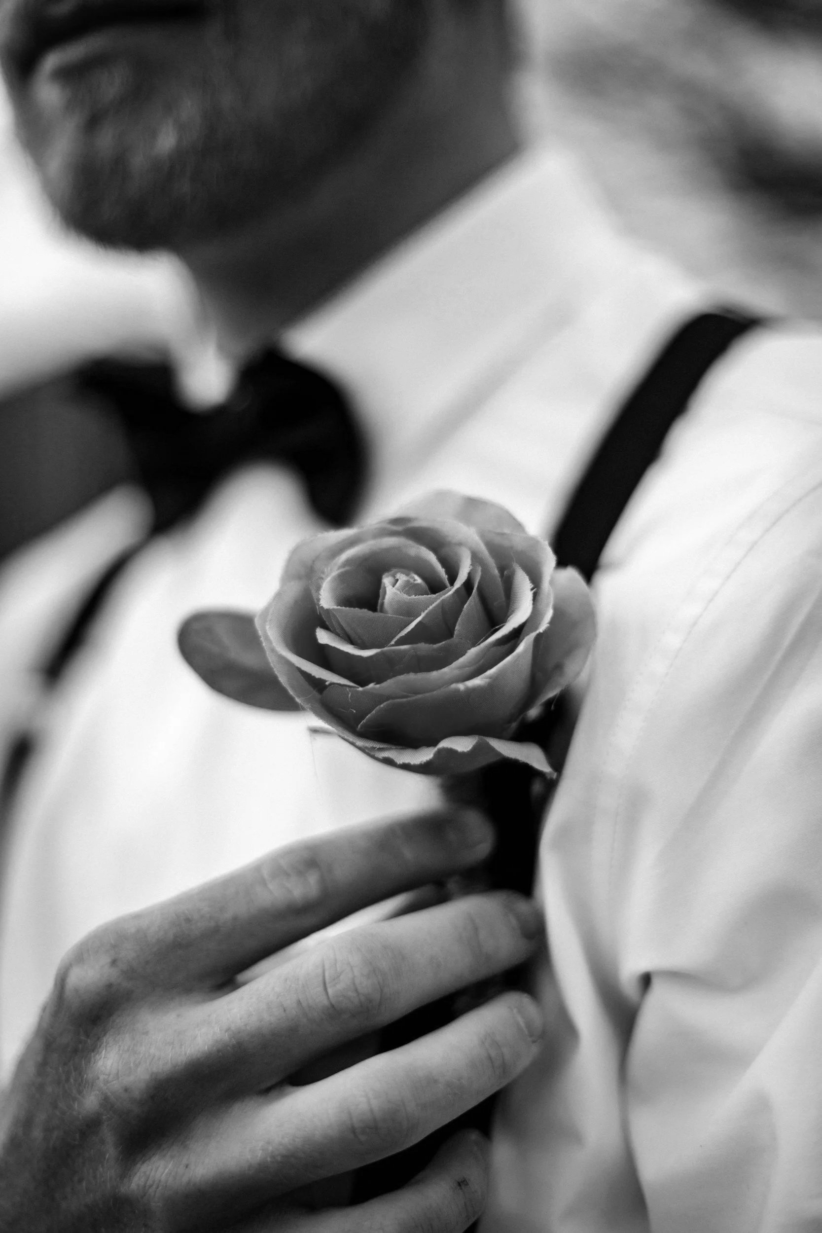 A man wearing a tuxedo holding a rose close to his chest.